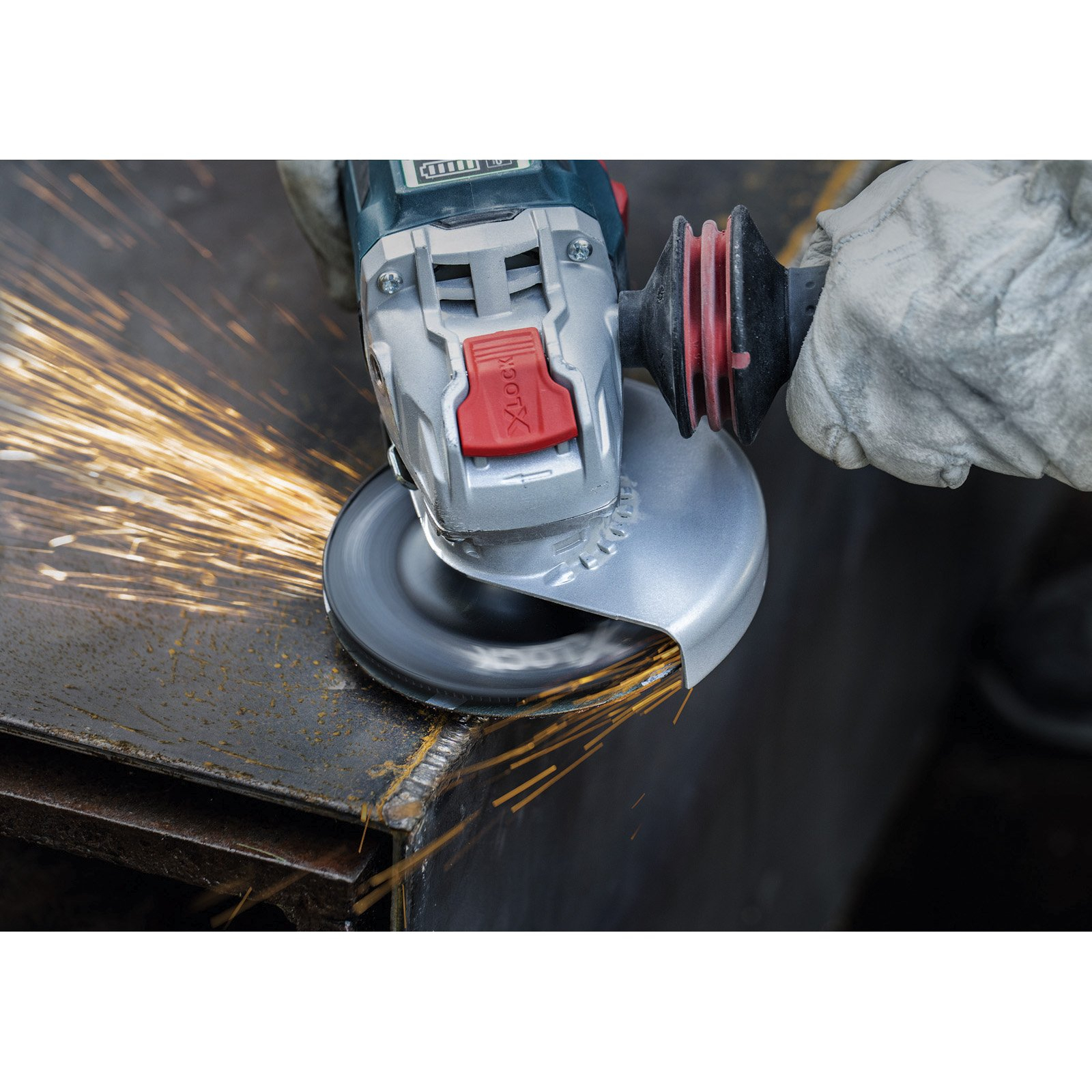 Ein Metallschleifer funkt beim Schneiden einer Metalloberfläche. Funken und Werkzeug im Vordergrund mit einem behandschuhten Arm. Dunkler Hintergrund.
