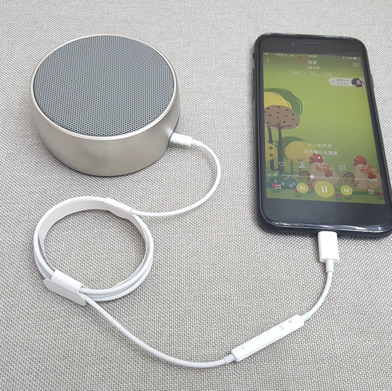 Ein silberner Lautsprecher neben einem Telefon, das Musik abspielt, verbunden durch ein weißes Kabel. Das Telefon zeigt einen grünen Hintergrund.