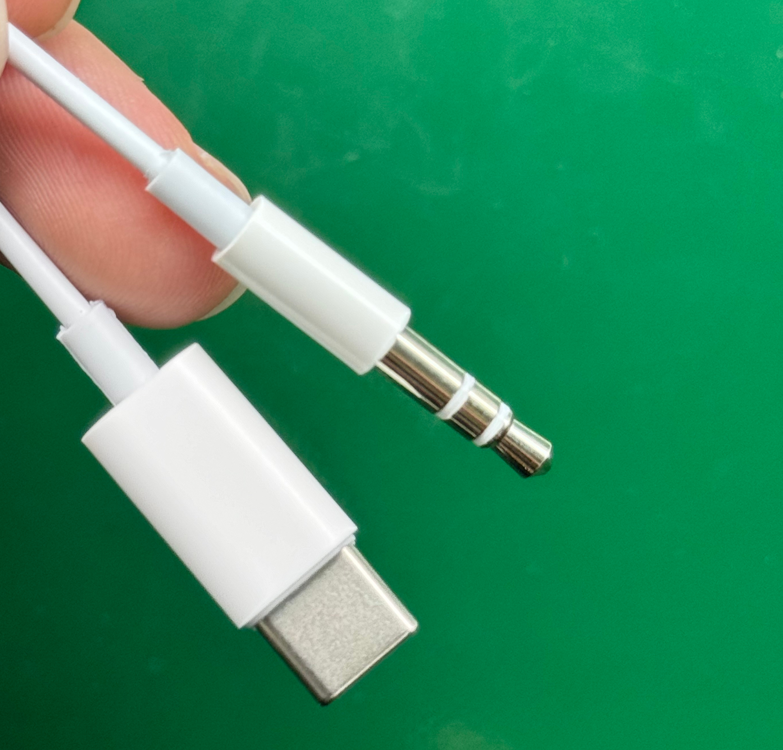 Weißes USB-C- und 3,5-mm-Audio-Jack-Kabel, das von einer Hand gehalten wird. Grüner Hintergrund.