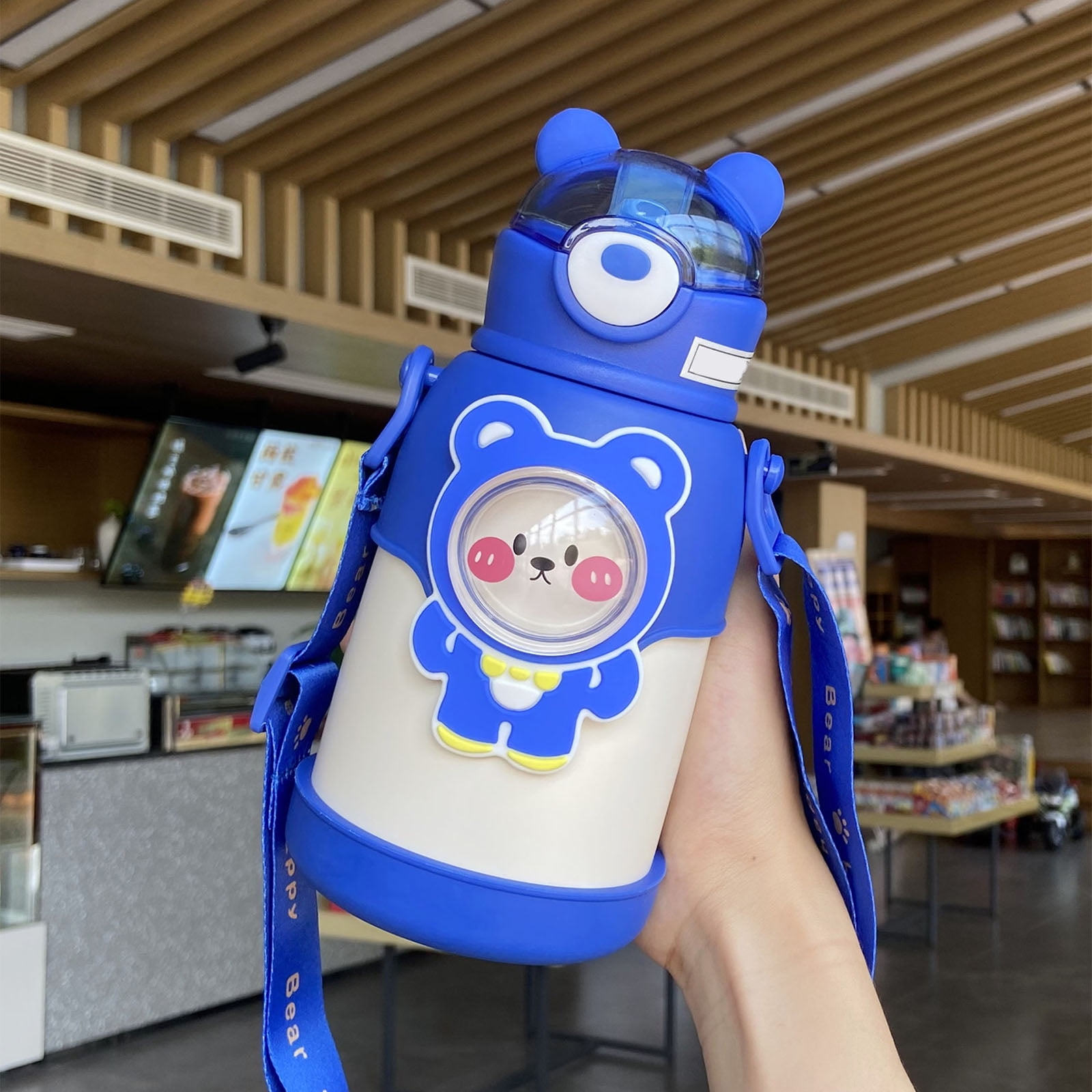 Blau-weiße, bärenförmige Wasserflasche, die von einer Person gehalten wird. Der Hintergrund hat Holzpaneele und ein Geschäft.