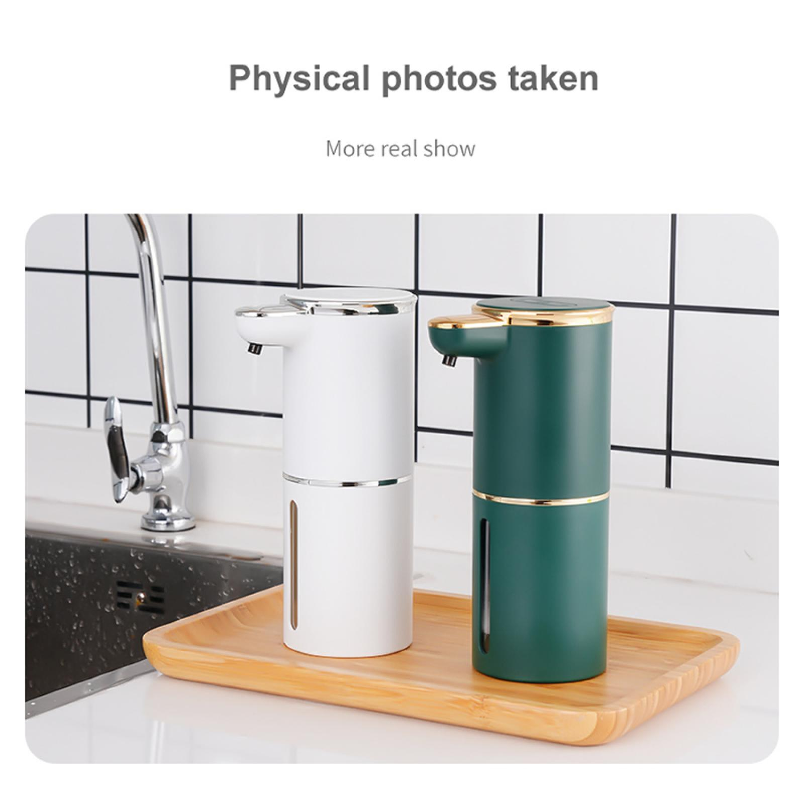 Zwei automatische Seifenspender, einer weiß und einer grün, auf einem Holztablett, mit Wasserhahn und Spüle im Hintergrund.