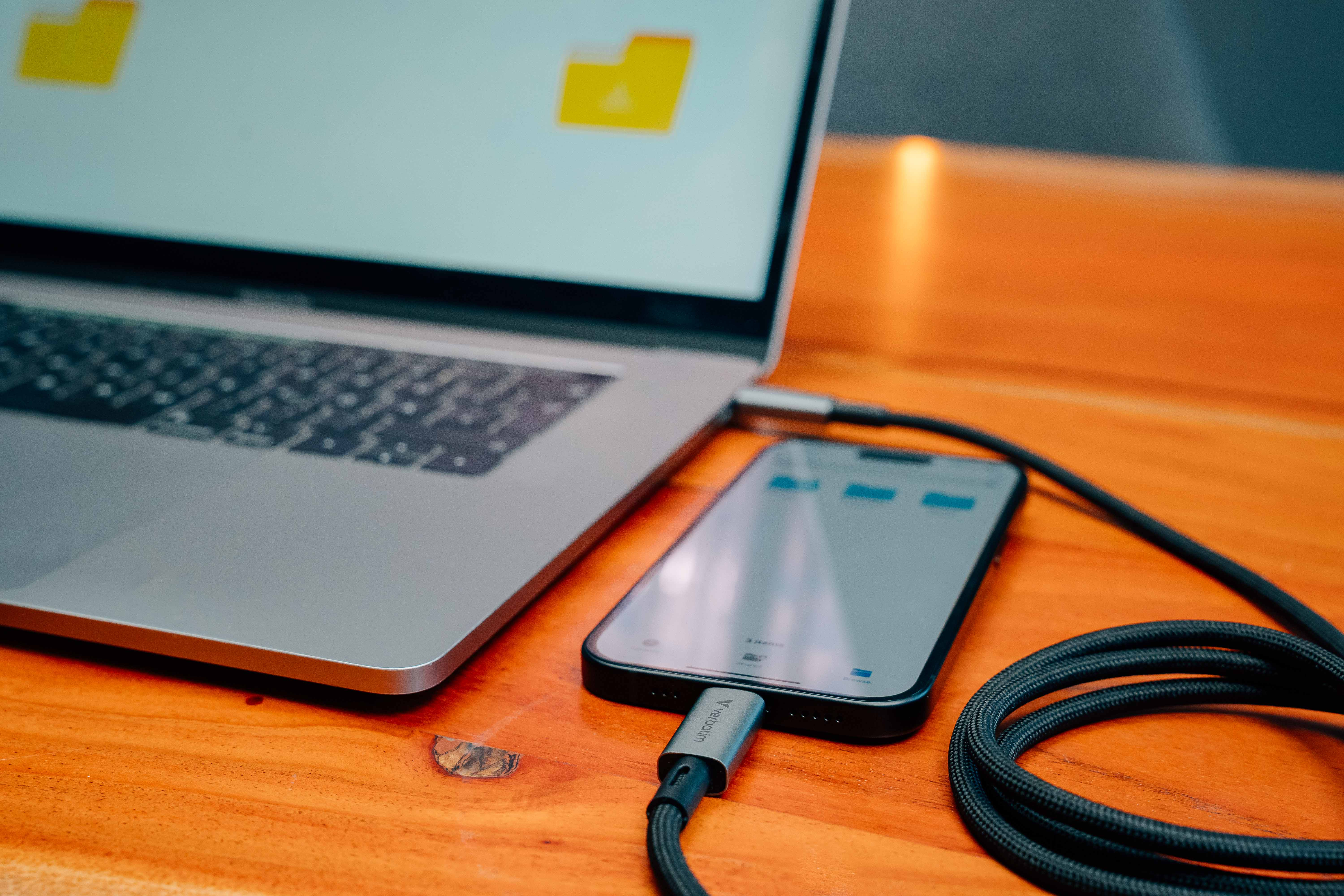 Ordinateur portable et téléphone connectés par un câble de chargement sur une table en bois. Le téléphone charge.
