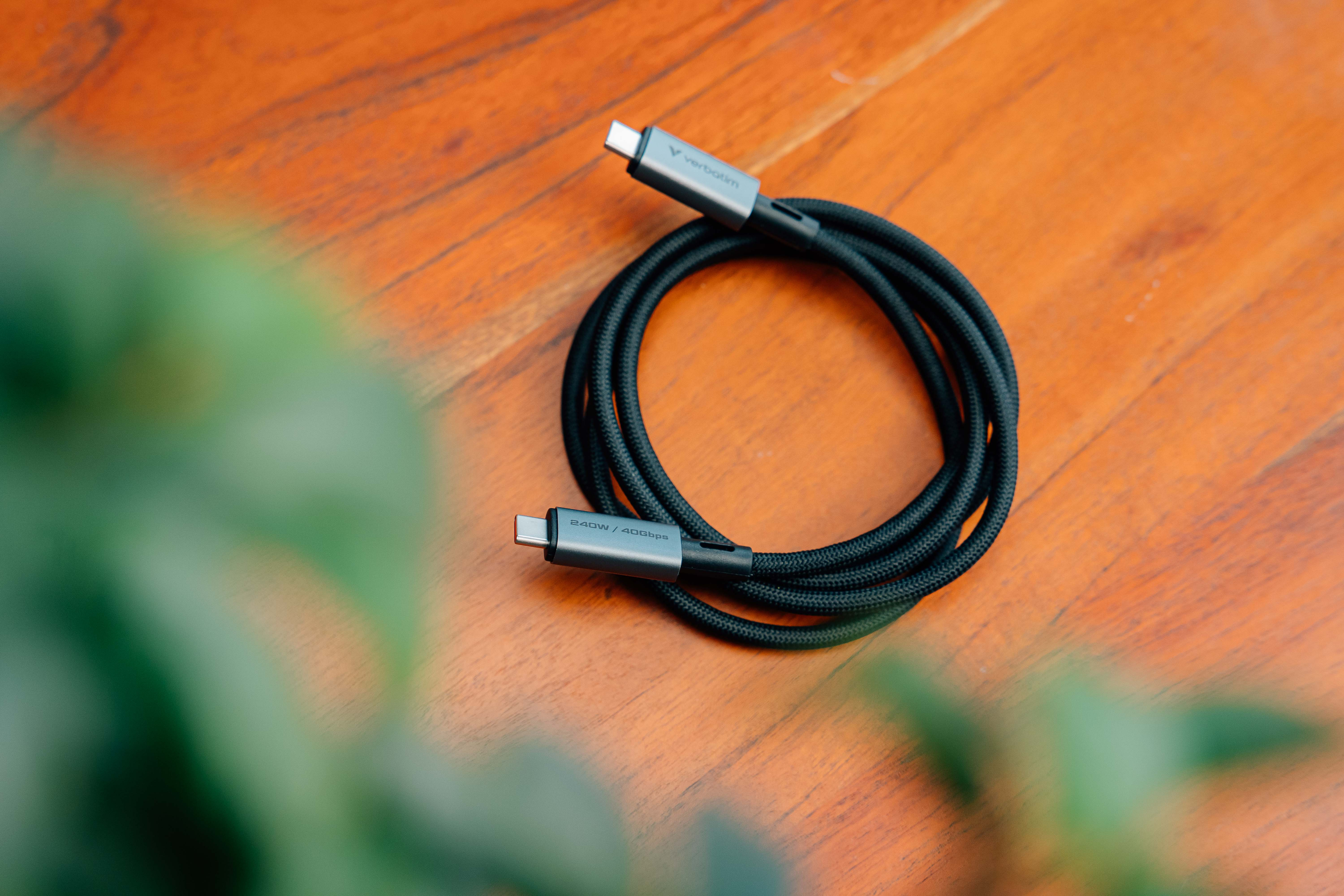 Un câble USB-C noir est enroulé sur une surface en bois. Le câble a des connecteurs argentés, et le fond est flou.