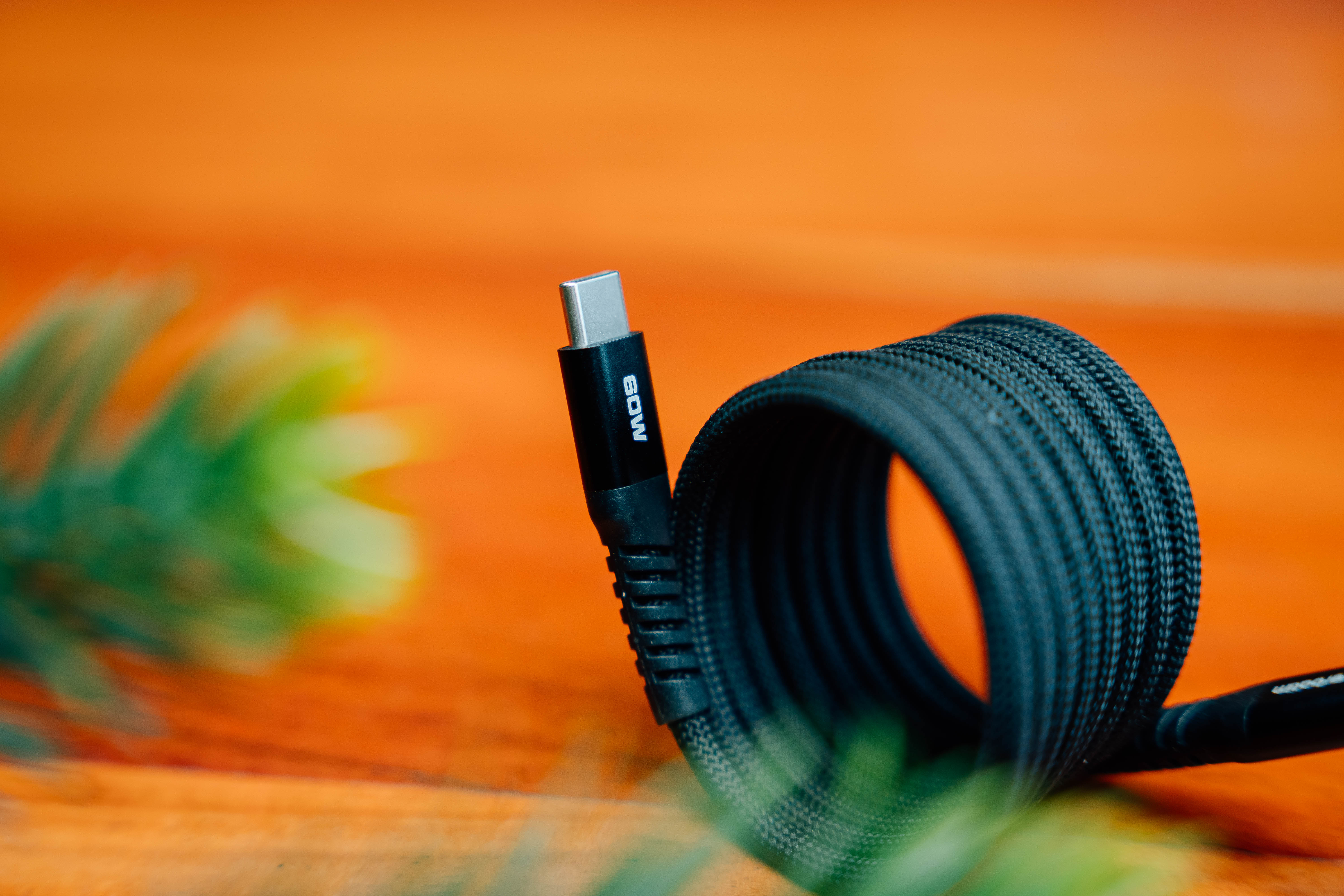 Zwarte USB-C-kabel op een oranje oppervlak. De kabel heeft een 60W-markering.