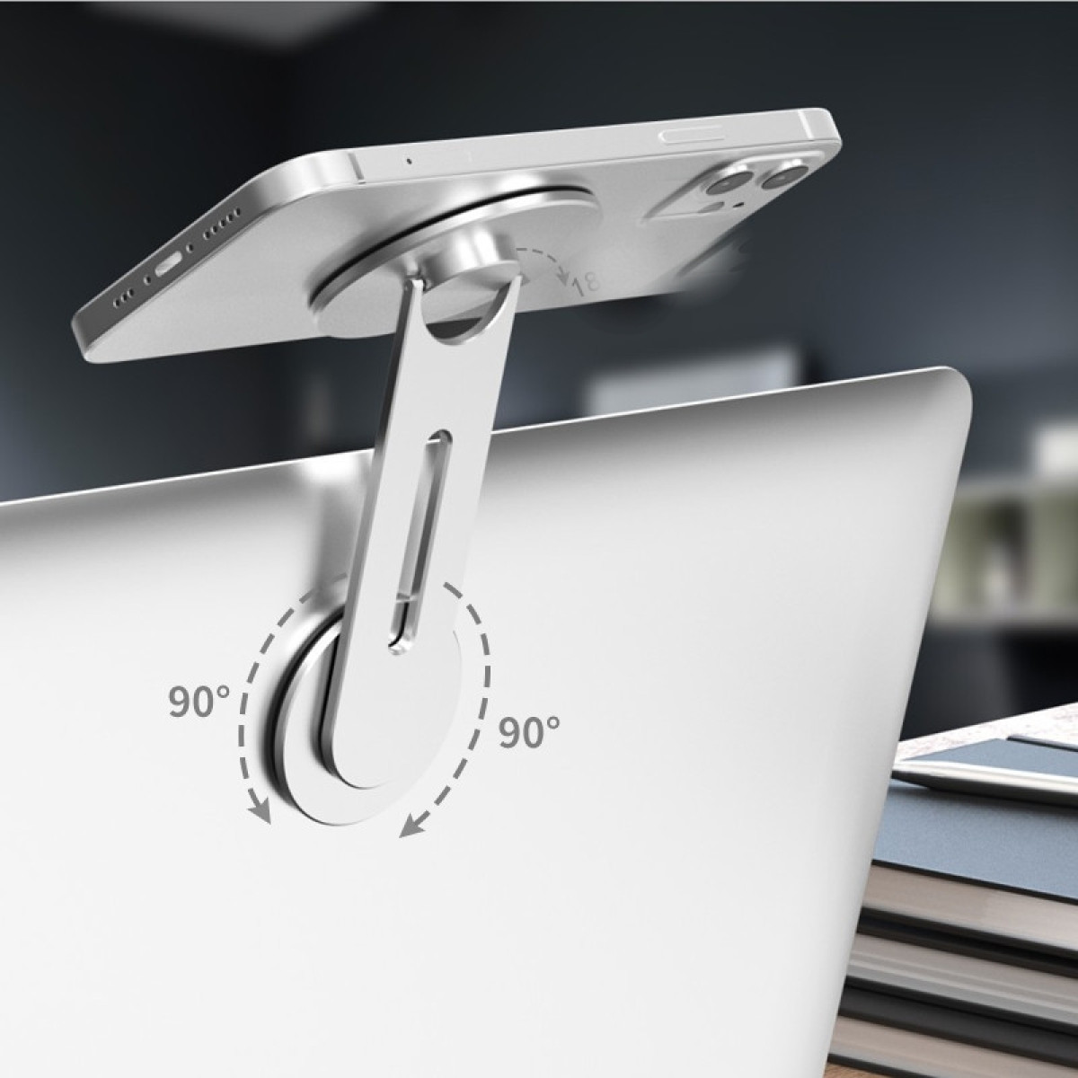 Srebrny telefon jest przymocowany do laptopa z obrotowym stojakiem. Stojak umożliwia obrót o 90 stopni. Książki w tle.