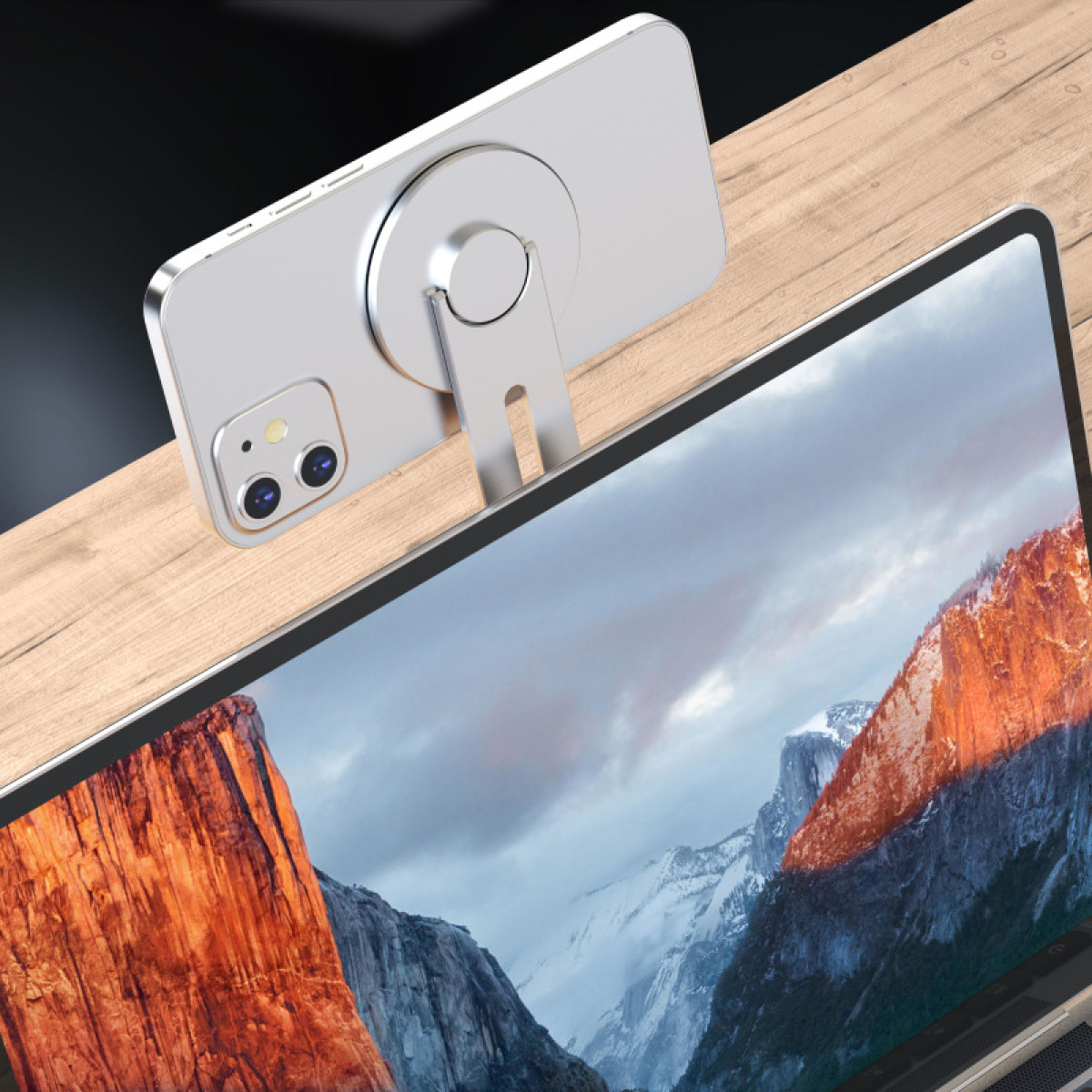 Srebrny telefon jest zamontowany na drewnianej powierzchni, nad laptopem wyświetlającym krajobraz górski. Telefon ma dwa aparaty.