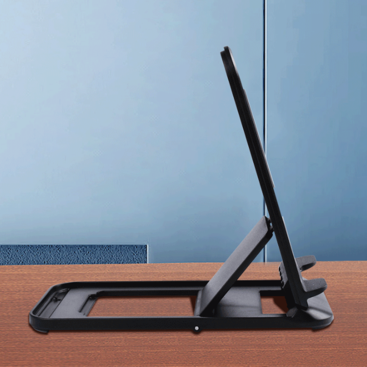 Czarny stojak na telefon na drewnianej powierzchni z niebieskim tłem ściany. Stojak jest otwarty i skierowany w górę.