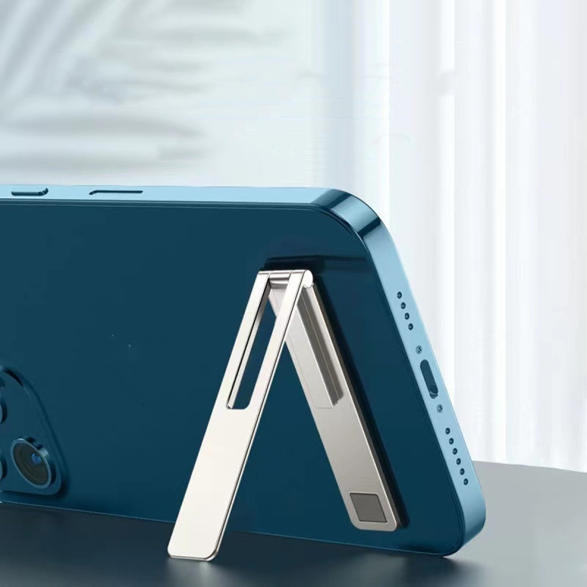 Niebieski telefon jest podparty srebrną podstawką. Podstawka jest ustawiona pod kątem, a telefon stoi na stole.