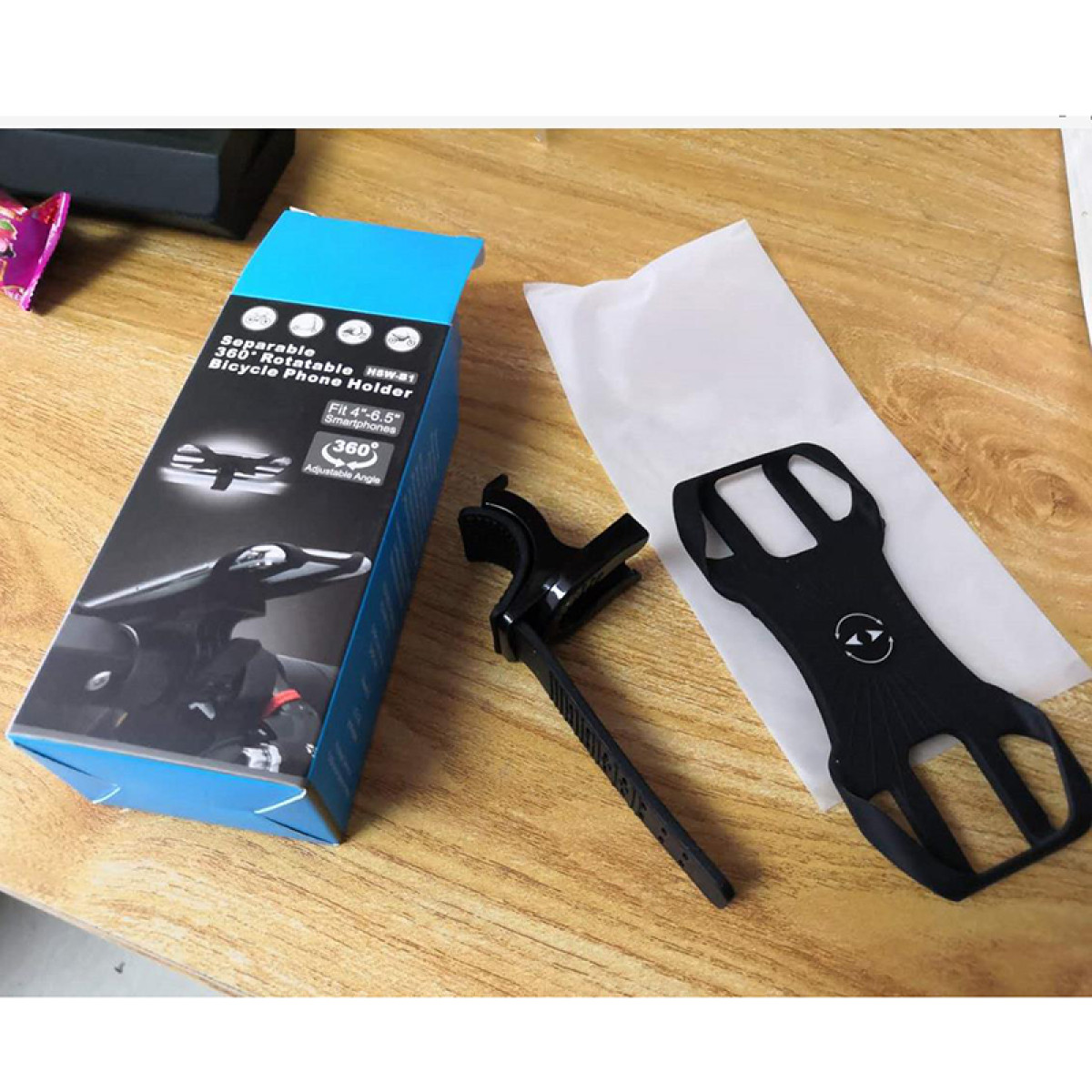 Zestaw uchwytu na telefon do roweru. Zawiera pudełko, czarny uchwyt, czarny wspornik i białą kartkę, wszystko na drewnianej powierzchni.