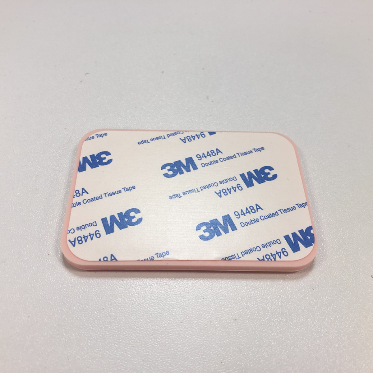 Prostokątna różowa podkładka samoprzylepna z białym tłem. Tło pokazuje logo 3M i tekst dla dwustronnej taśmy z tkaniny.