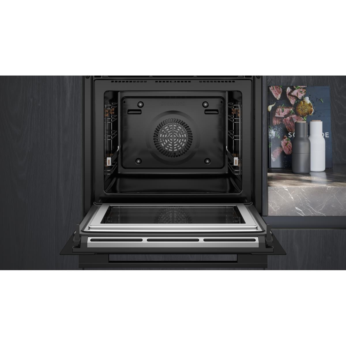 Een open zwarte oven met glazen deur. Een kookboek en zout/peper strooiers staan rechts.