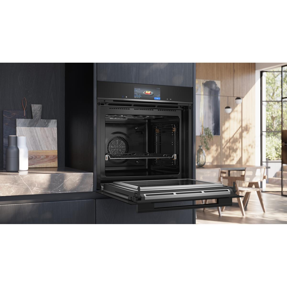 Een moderne oven met een open deur, die het interieur onthult. De achtergrond toont een eethoek met tafel, stoelen en een raam.