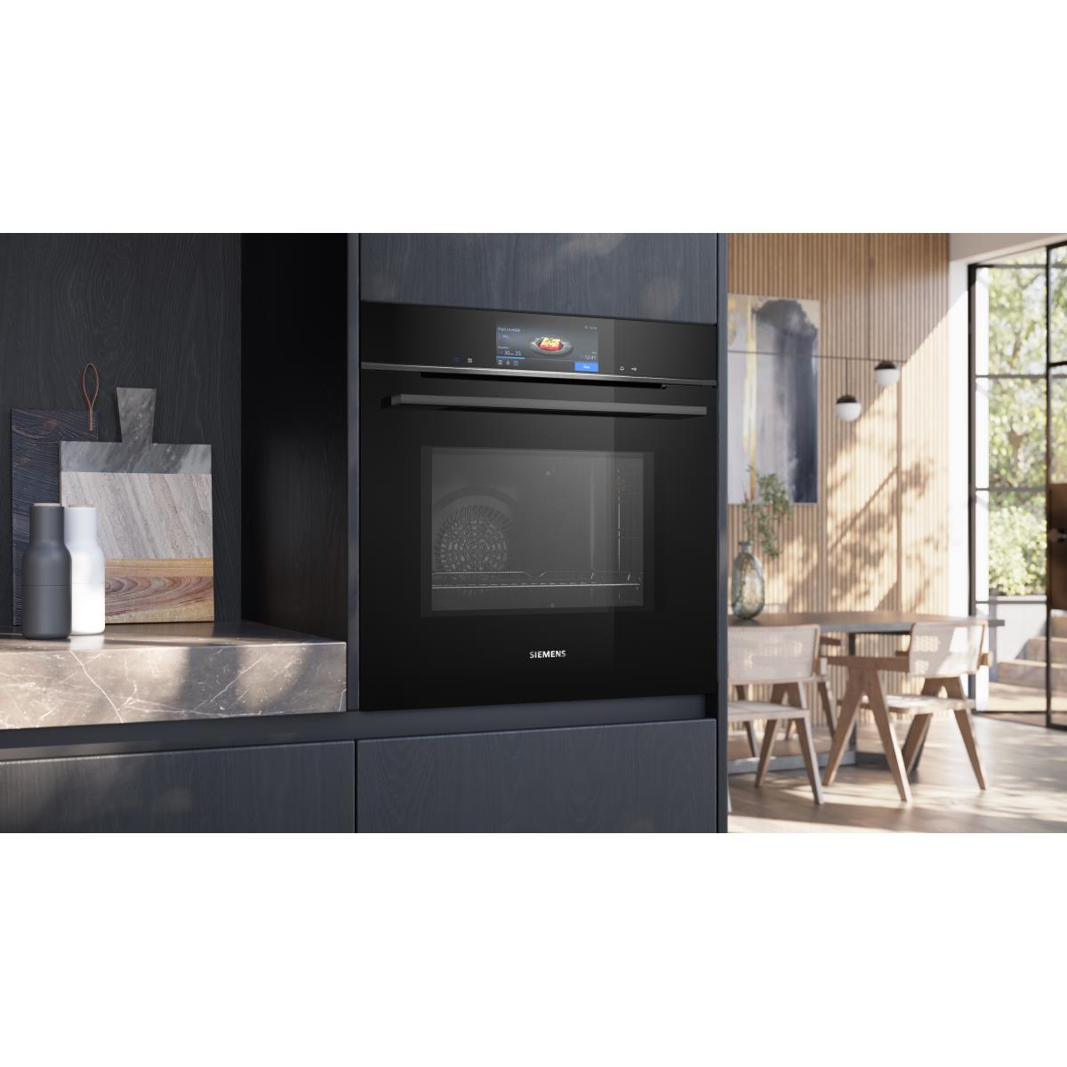 Een ingebouwde zwarte oven met een digitaal display staat centraal. Een eethoek met tafel en stoelen is zichtbaar op de achtergrond.