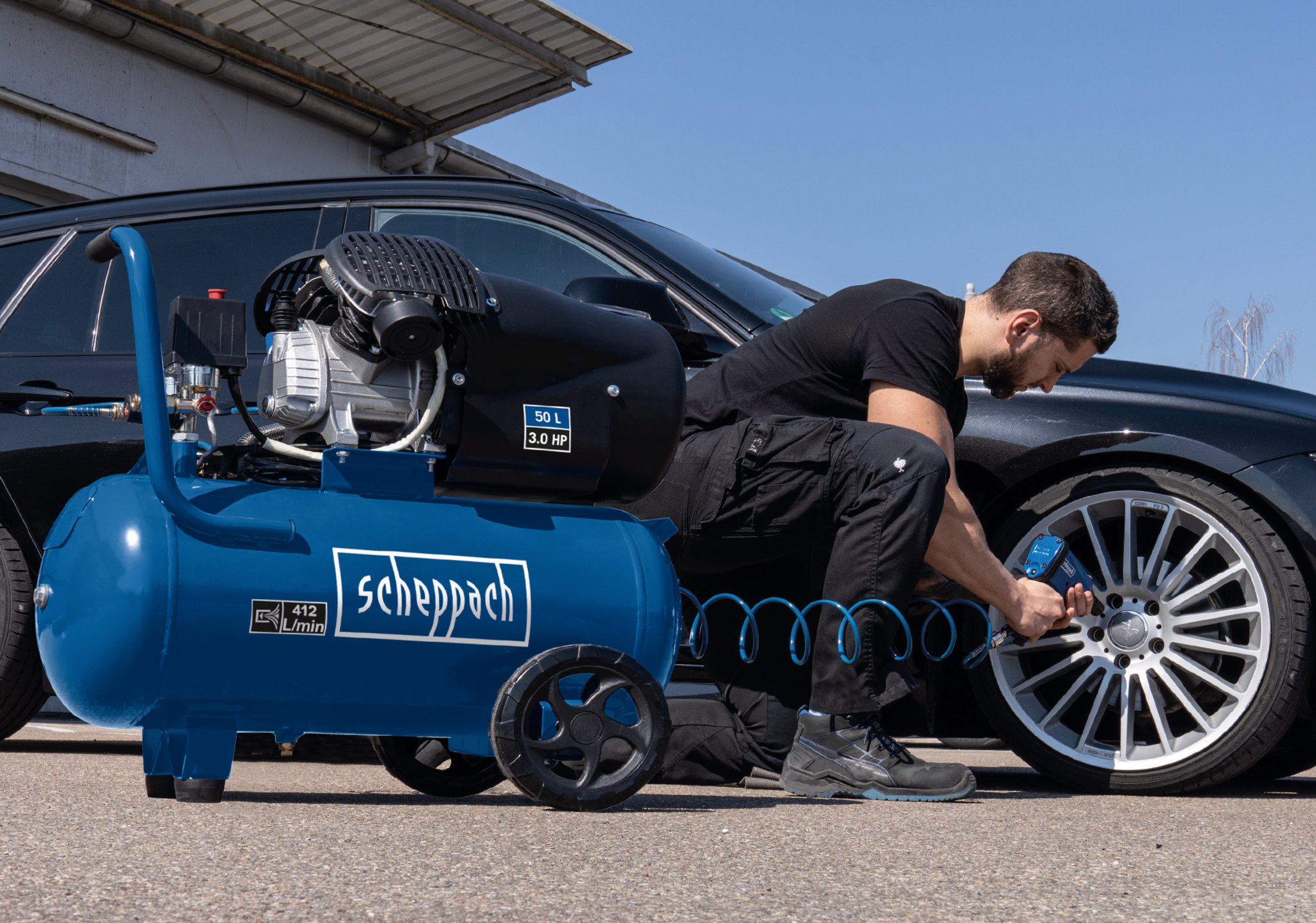 Uomo usa un compressore per gonfiare pneumatico auto. Compressore blu a sinistra, auto nera a destra.