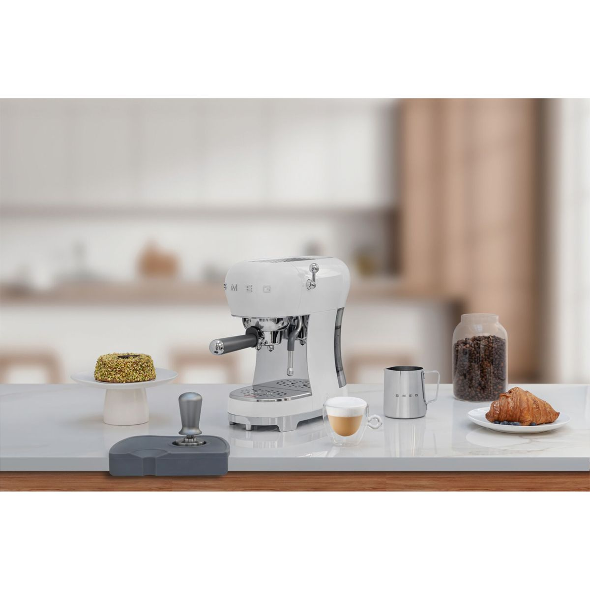 Weiße Espressomaschine auf einer Theke mit Kaffee, Kuchen und Croissant. Der Hintergrund ist unscharf.