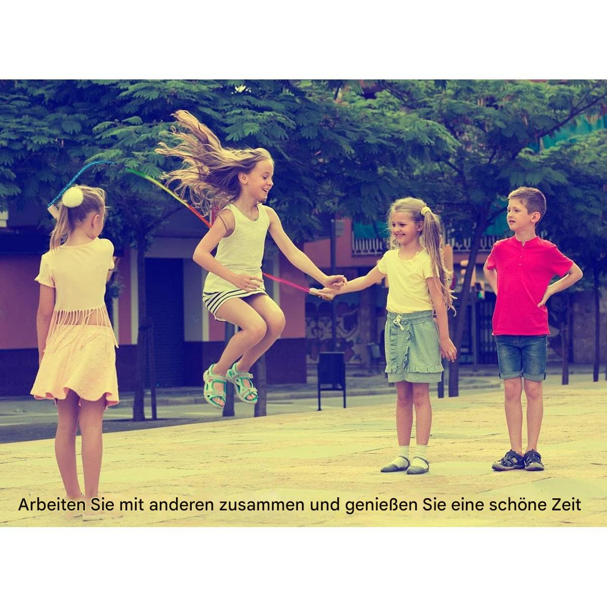 Vier Kinder spielen draußen Seilspringen. Ein Mädchen springt, während zwei andere das Seil halten. Ein Junge steht und schaut zu.