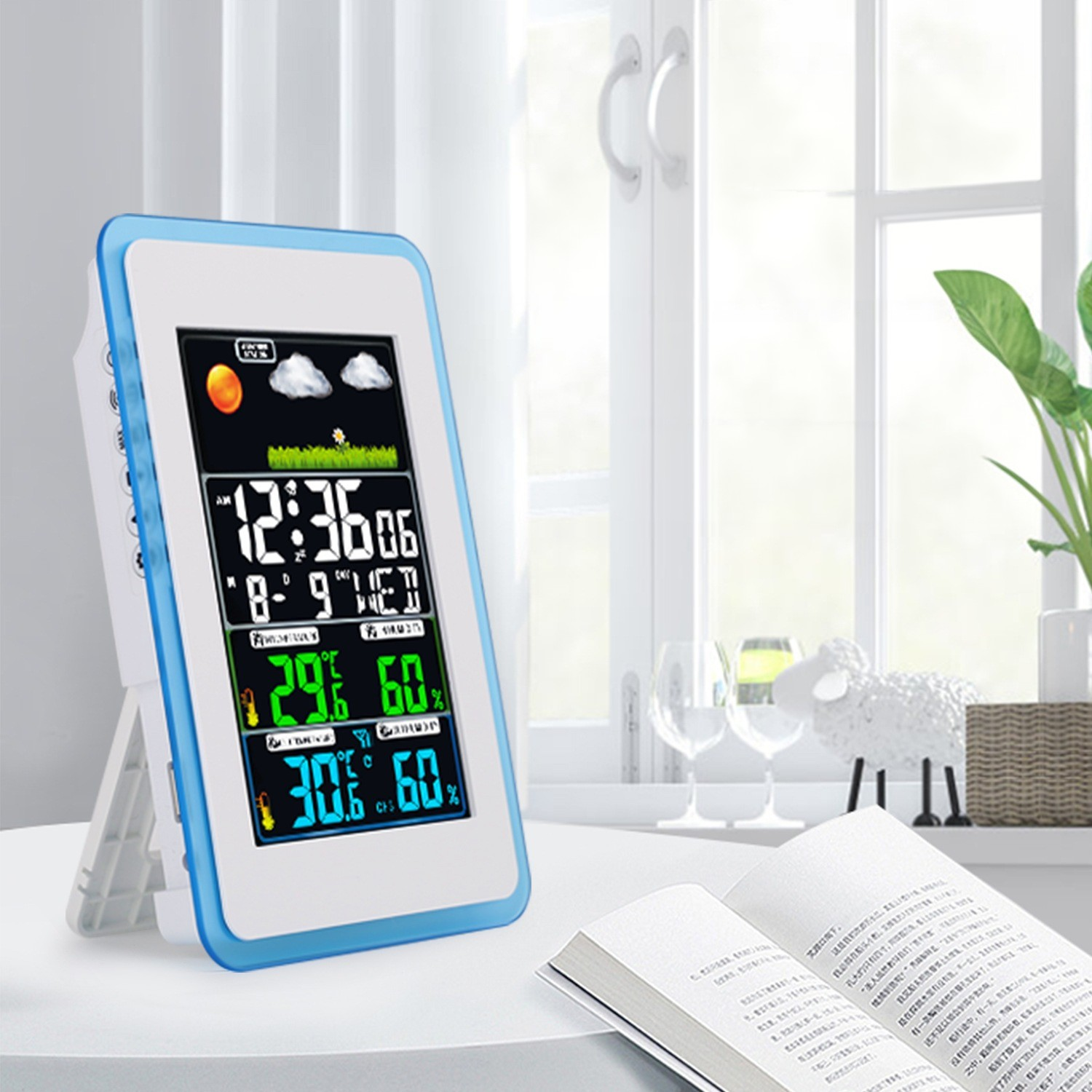 Eine Wetterstation zeigt Zeit, Temperatur und Luftfeuchtigkeit an. Ein Buch und ein dekoratives Schaf stehen auf einem Tisch am Fenster.
