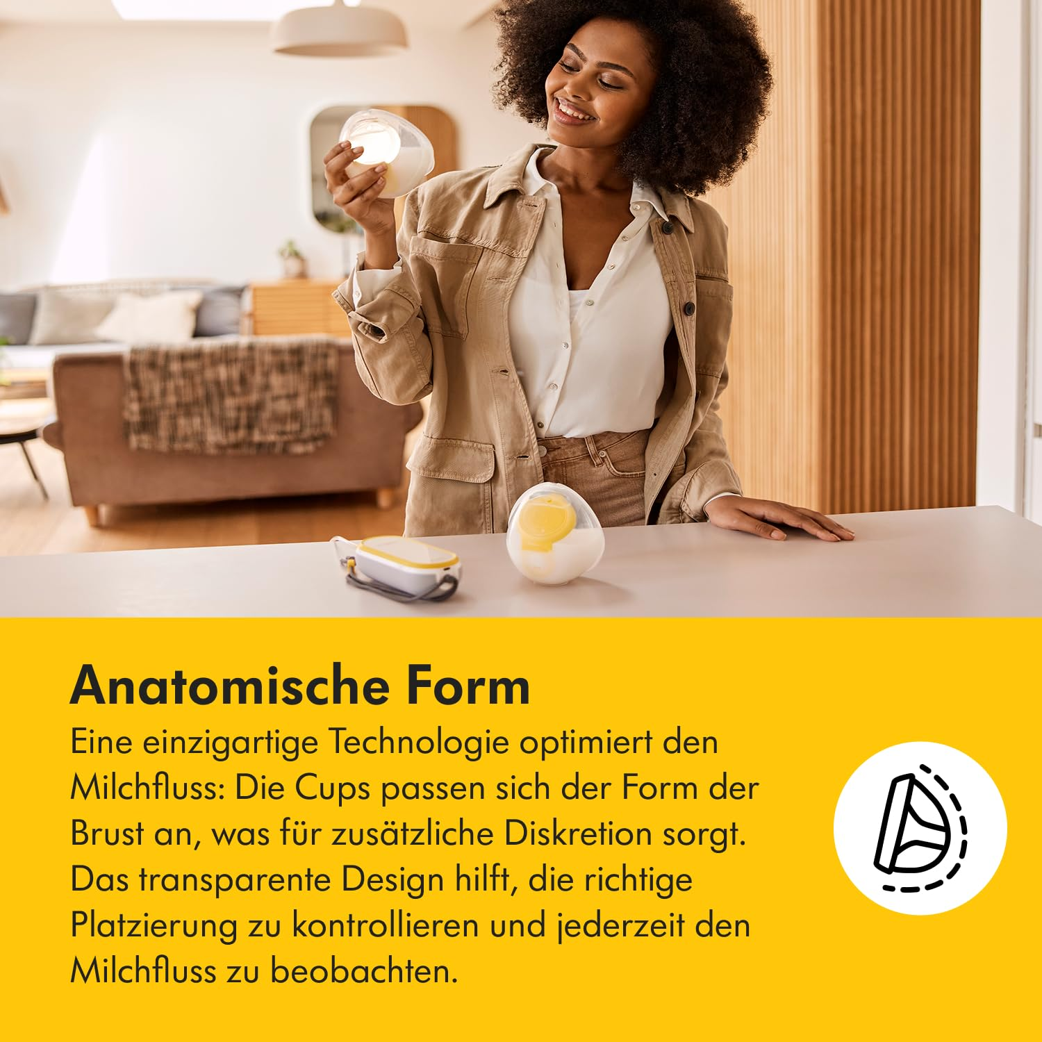 Eine Frau hält ein Brustpumpenteil und lächelt. Auf dem Tisch liegt ein weiteres Teil. Der Hintergrund zeigt ein Wohnzimmer.