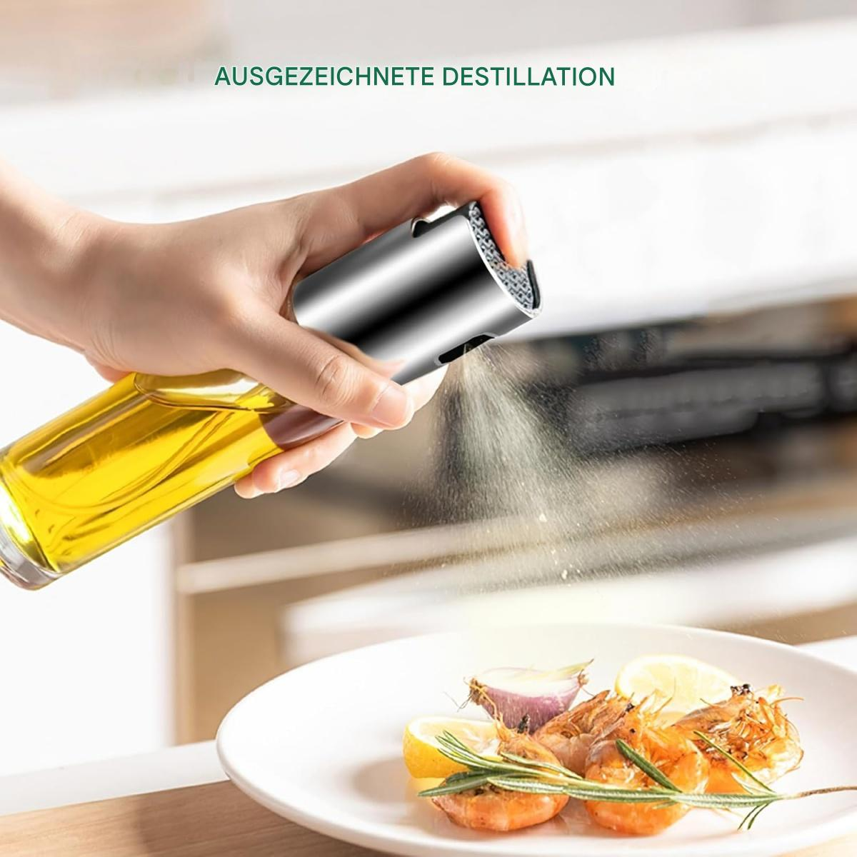 Eine Hand sprüht Öl auf einen Teller mit Garnelen, Zitrone und Knoblauch. Die Ölflasche ist klar, der Sprüher silbern.