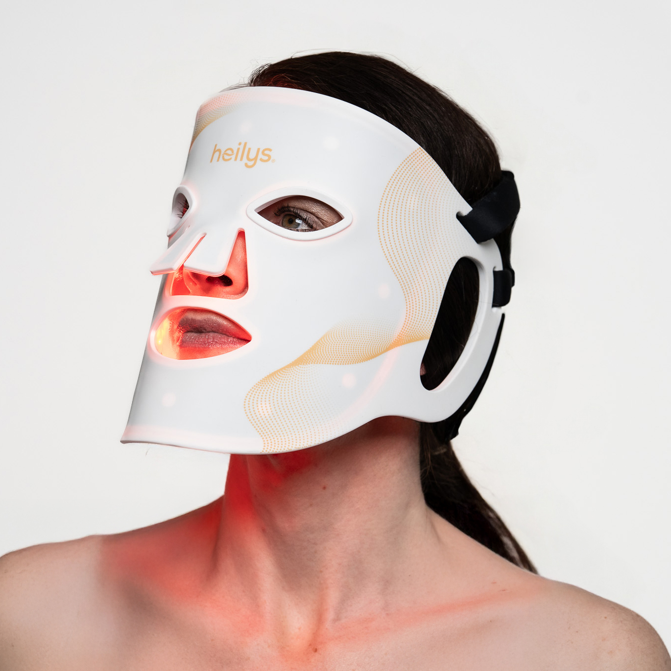 Eine Person trägt eine weiße LED-Gesichtsmaske. Die Maske beleuchtet das Gesicht mit rotem Licht. Der Hintergrund ist weiß.