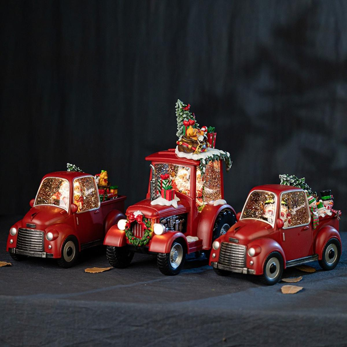 Drei rote Spielzeug-Lkw, die für Weihnachten geschmückt sind. Der mittlere ist ein Traktor. Jeder hat Geschenke und Schnee. Dunkler Hintergrund.