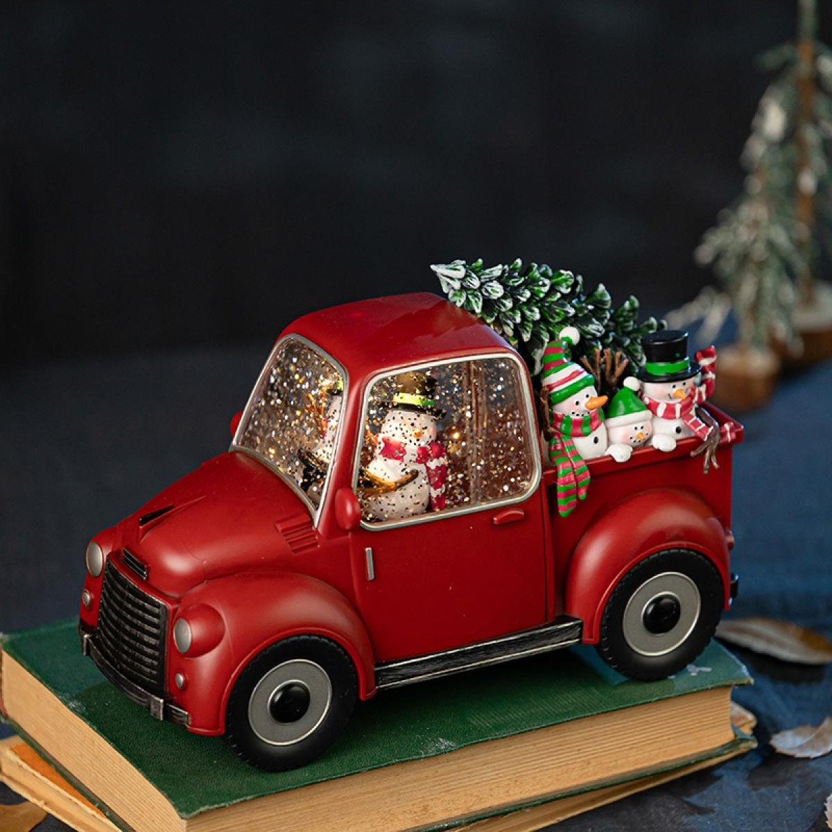 Ein rotes Spielzeugauto mit Schneemännern im Inneren und auf der Rückseite, mit einem Weihnachtsbaum. Es steht auf einem Bücherstapel.
