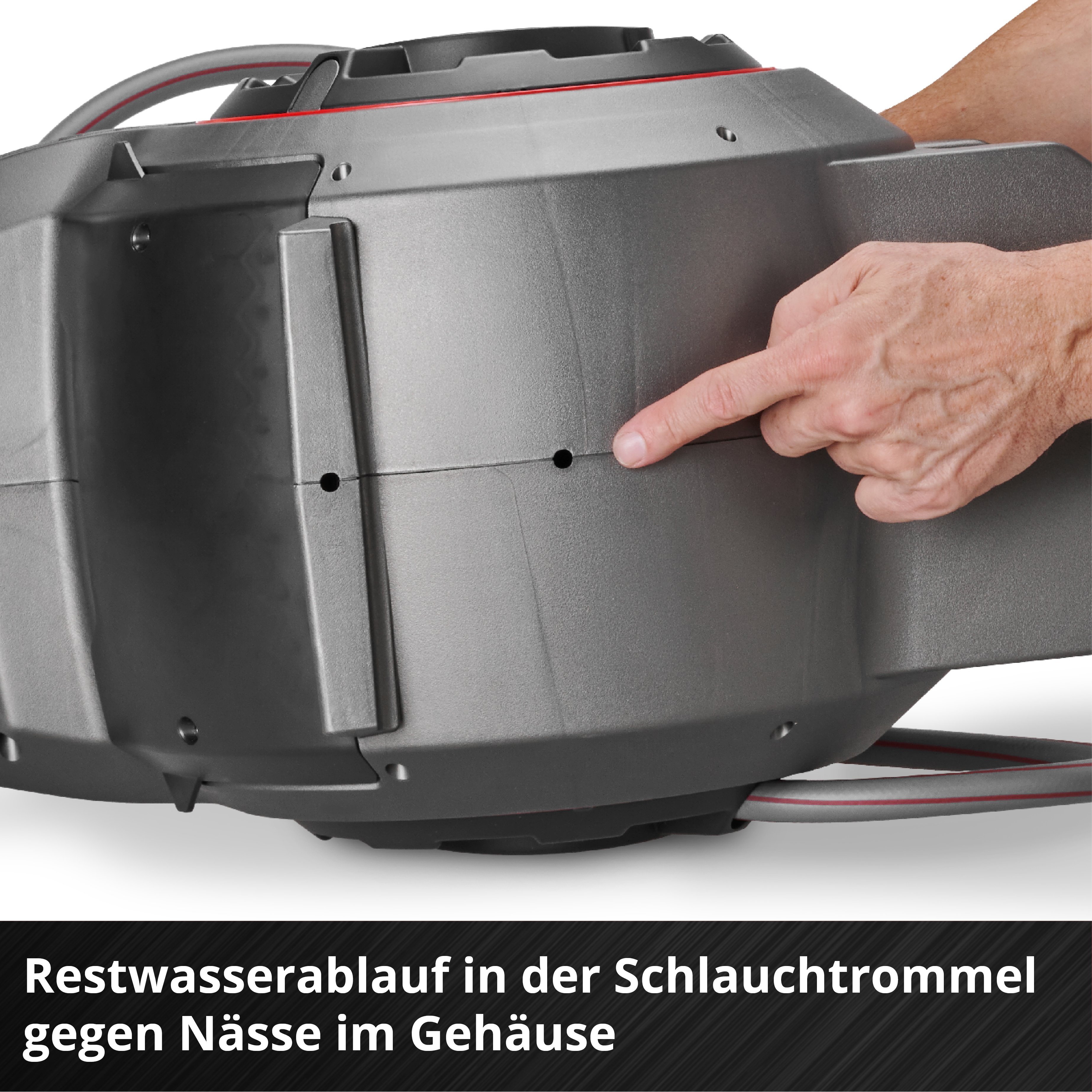 Ein Finger zeigt auf ein Loch an einer grauen Schlauchtrommel. Die Trommel hat einen roten Streifen. Text unten.