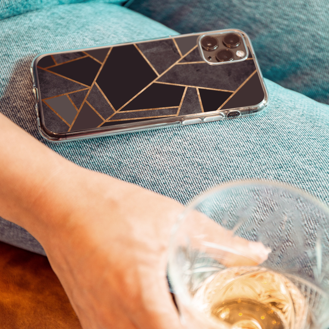 Telefoon met geometrisch ontwerp op schoot, een hand die een glas drank vasthoudt. Jeans op de achtergrond.