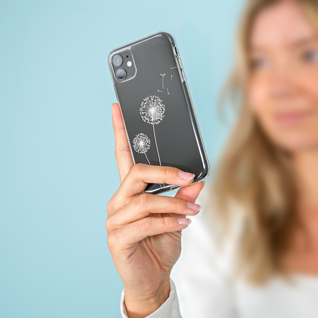 Een vrouw houdt een telefoon vast met een paardenbloemhoesje. De telefoon is zwart met witte paardenbloemontwerpen. Blauwe achtergrond.