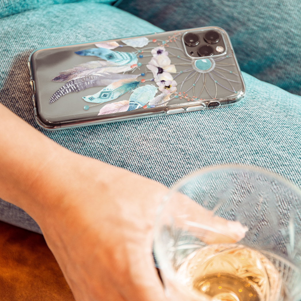 Une personne tenant un verre de vin, téléphone avec étui attrape-rêves sur un jean. Focus sur le téléphone et le verre.