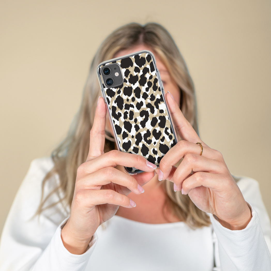 Femme tenant un téléphone avec une coque à imprimé léopard, mains au premier plan. Le fond est un mur beige flou.