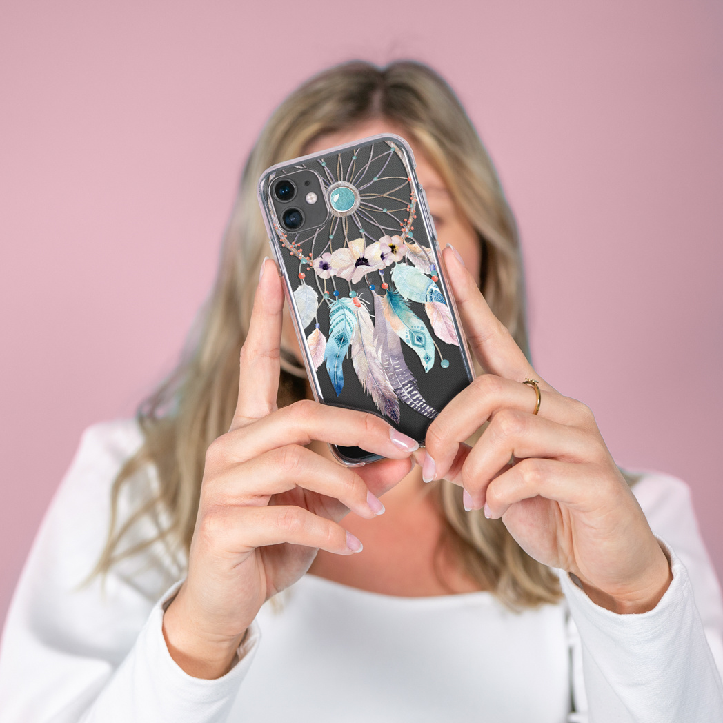 Una donna tiene in mano un telefono con un design acchiappasogni. La custodia del telefono ha piume blu, verde acqua e viola su sfondo nero.