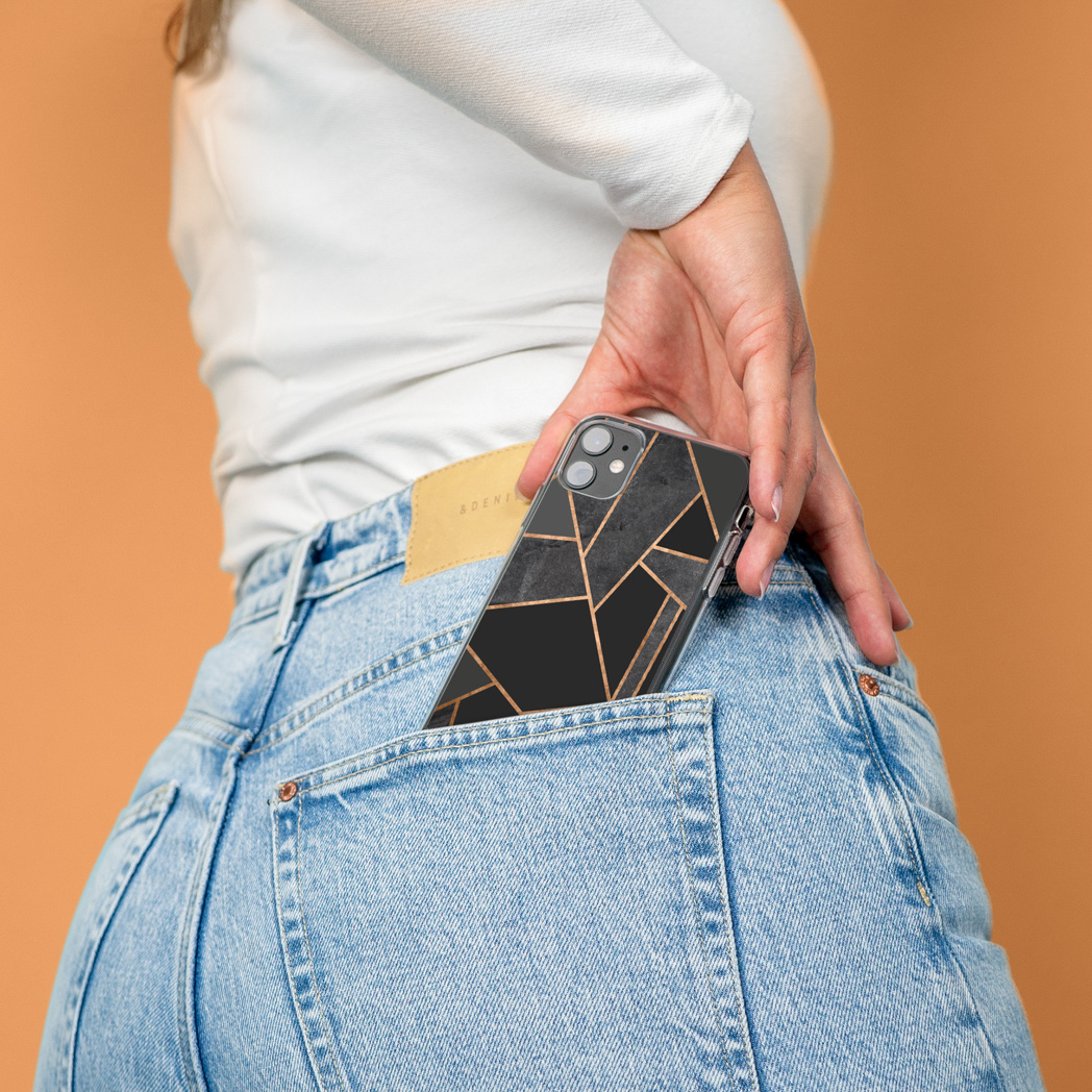 Una persona mette un telefono con una custodia dal design geometrico nella tasca posteriore di jeans blu. Sfondo arancione.