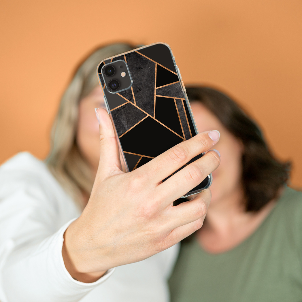 Una persona tiene in mano un telefono con un design geometrico nero e oro. Altre due persone sullo sfondo sfocato.