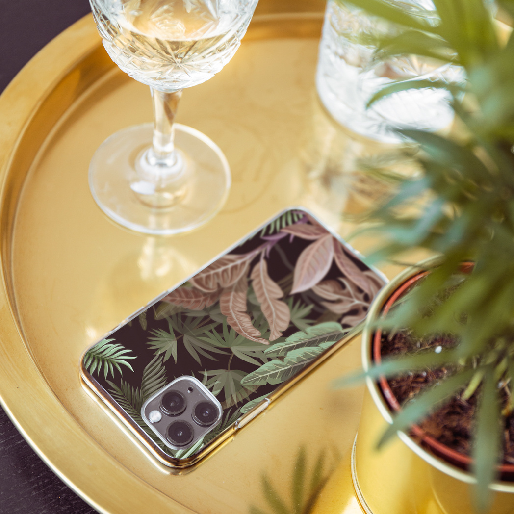 Vassoio dorato con telefono con disegno a foglie, bicchiere di vino e piccola pianta in vaso. Il vassoio riflette la luce.