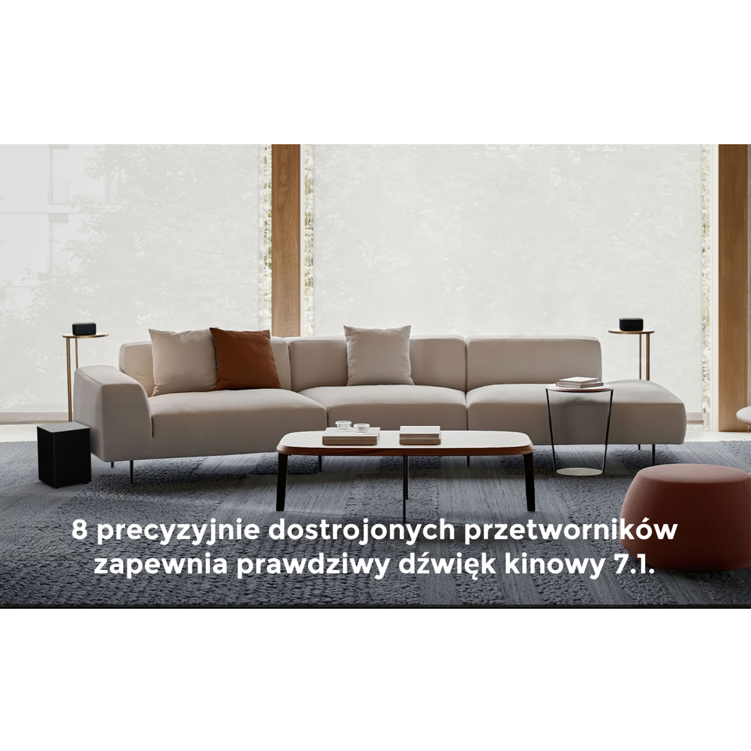 Nowoczesny salon. Duża beżowa sofa, czarne głośniki i stolik kawowy przed oknem. Tekst: dźwięk 7.1.