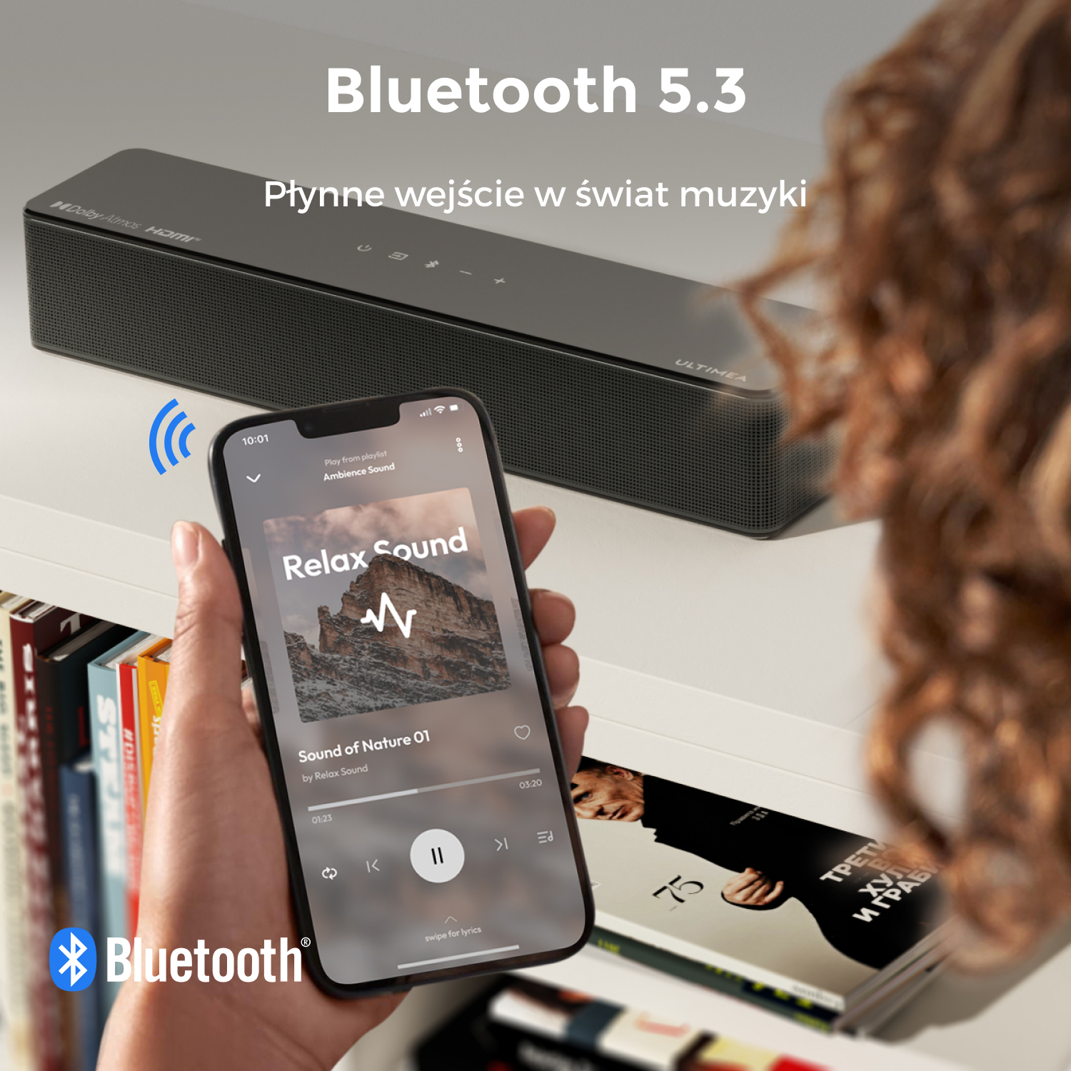 Osoba trzymająca telefon z muzyką. Czarny soundbar za telefonem. Logo Bluetooth na pierwszym planie.