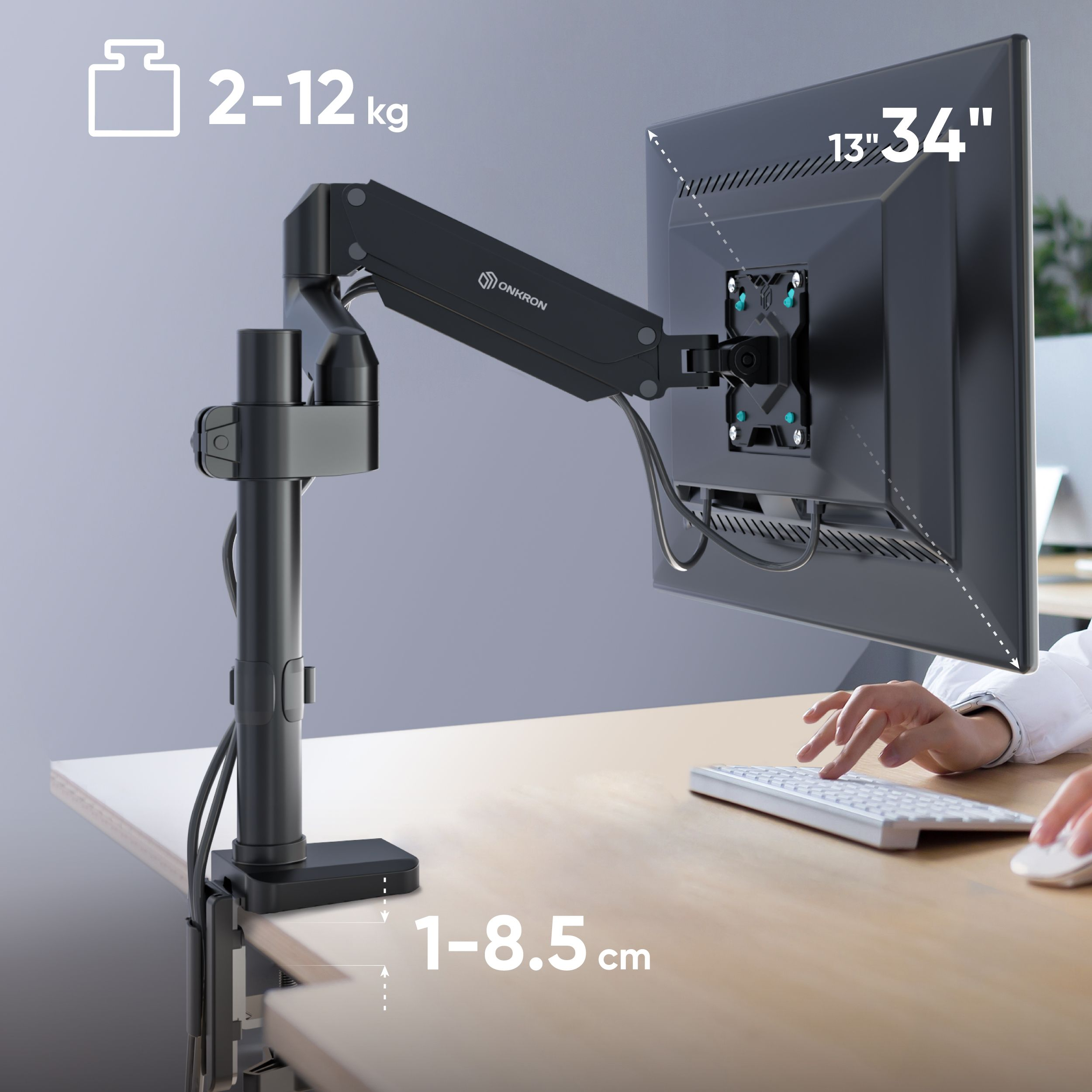 Ramię monitora z monitorem i klawiaturą na drewnianym biurku. Ramię jest czarne, monitor jest czarny, a klawiatura biała.