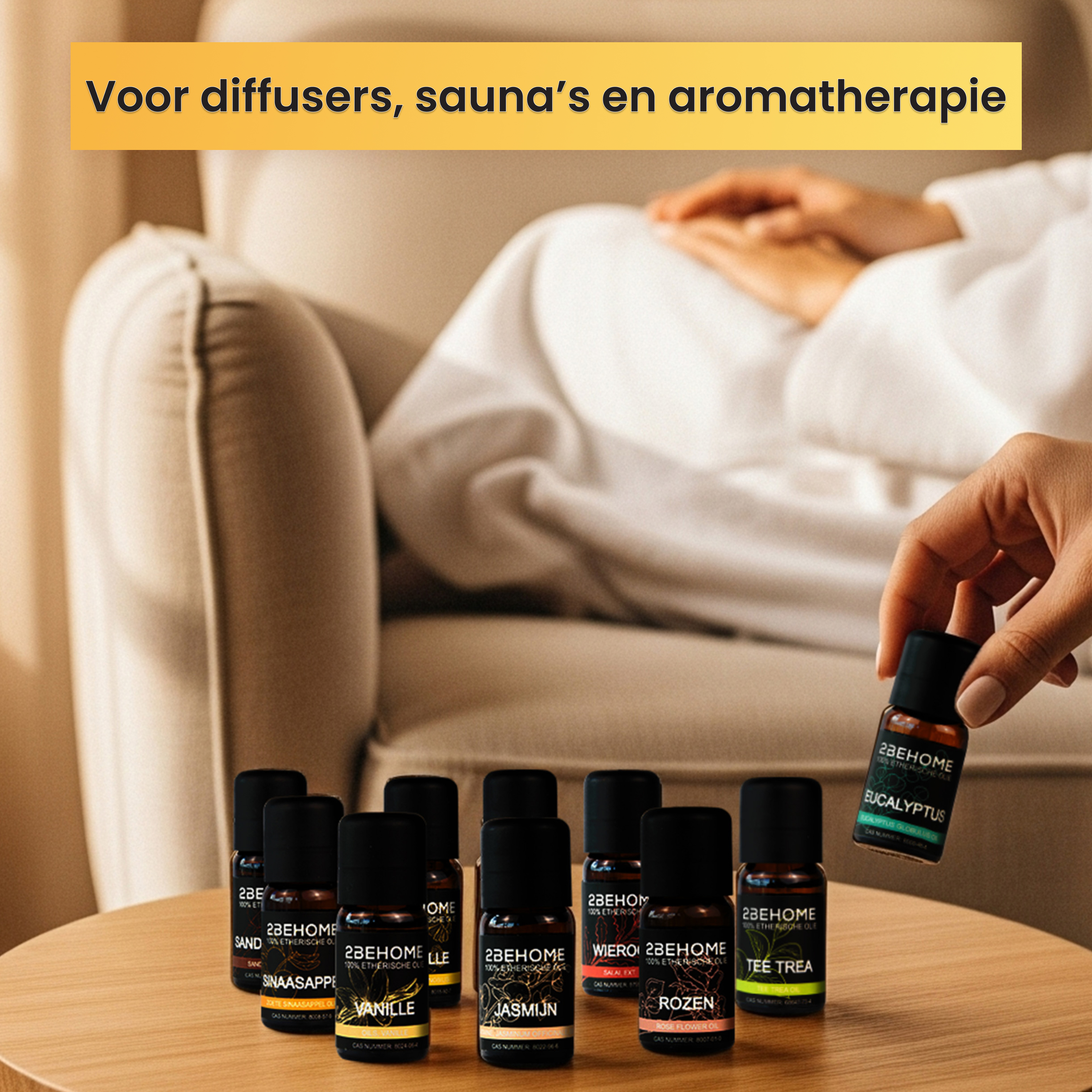 Image shows aromatherapy oils. A hand holds a bottle. Other bottles are on a wooden table. A person is seated in the background.