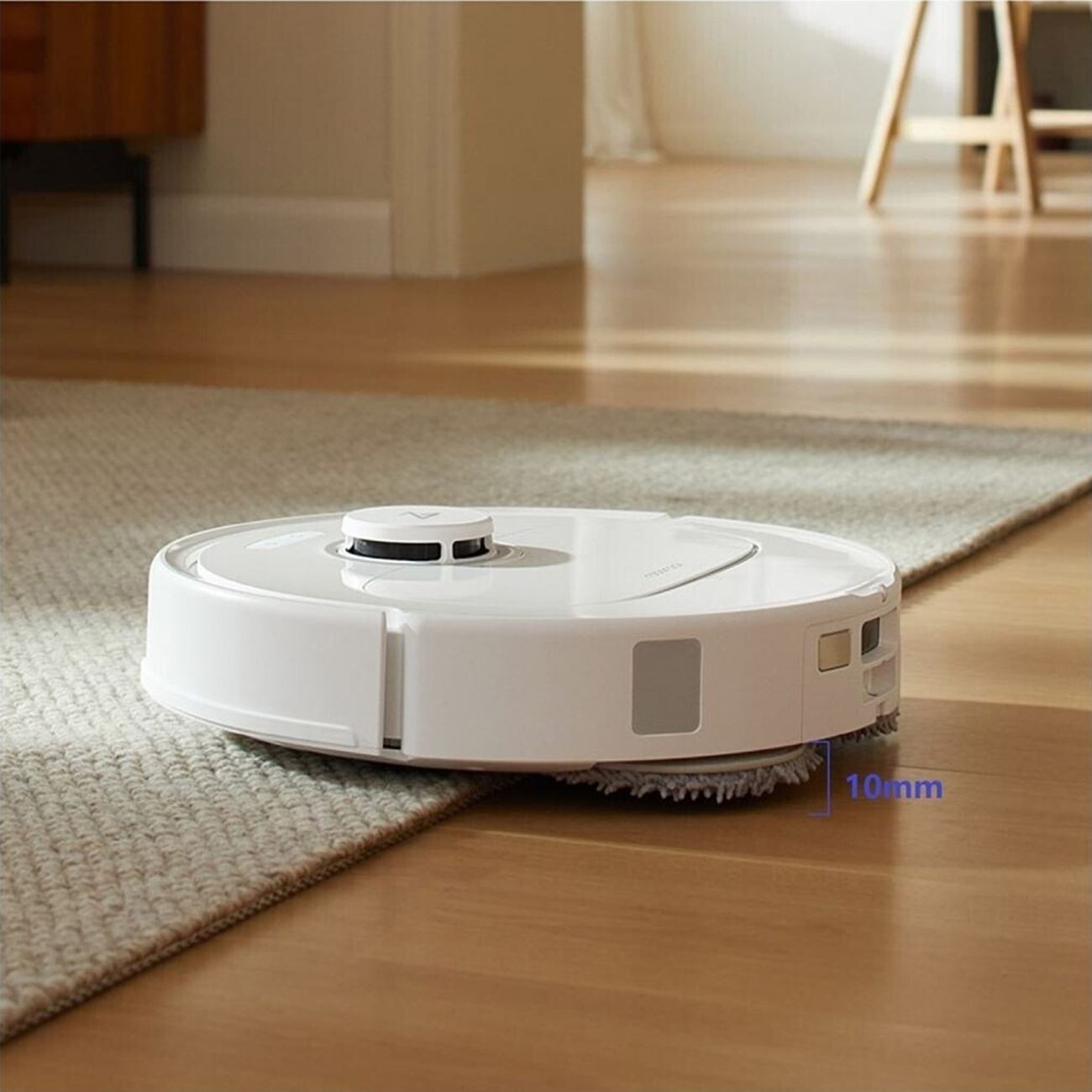 Biały robot odkurzający na drewnianej podłodze i dywanie. Urządzenie ma okrągły kształt i znajduje się na środku sceny.