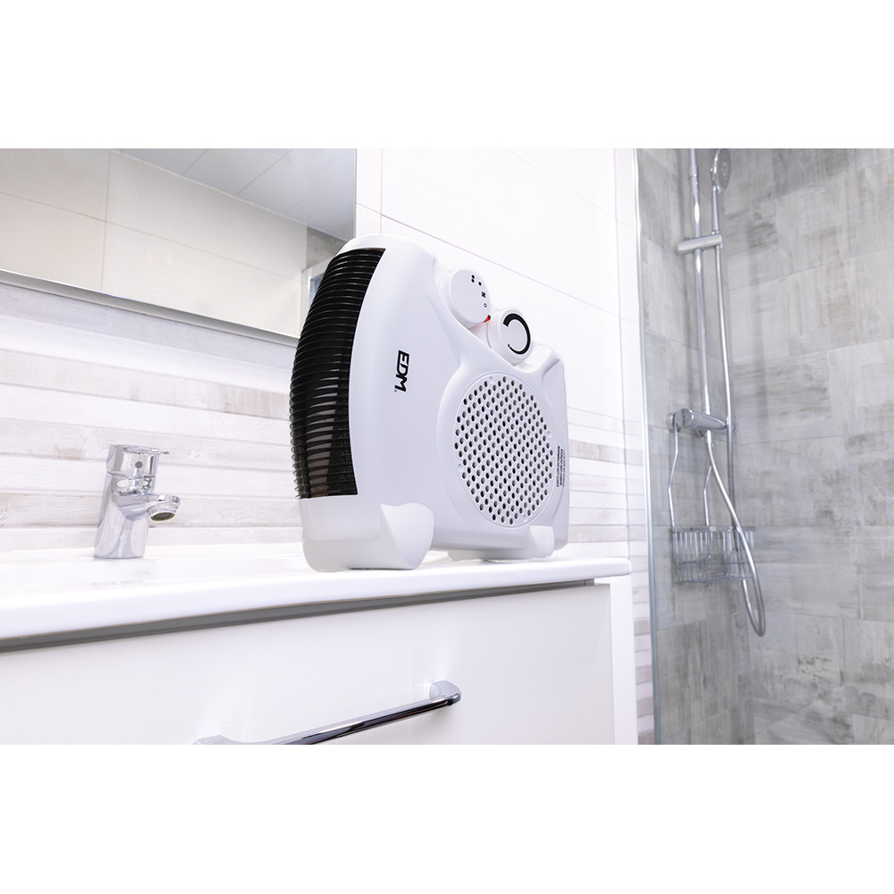 Un calefactor eléctrico blanco está sobre un lavabo blanco en un baño. Hay un grifo a la izquierda. La ducha está a la derecha.