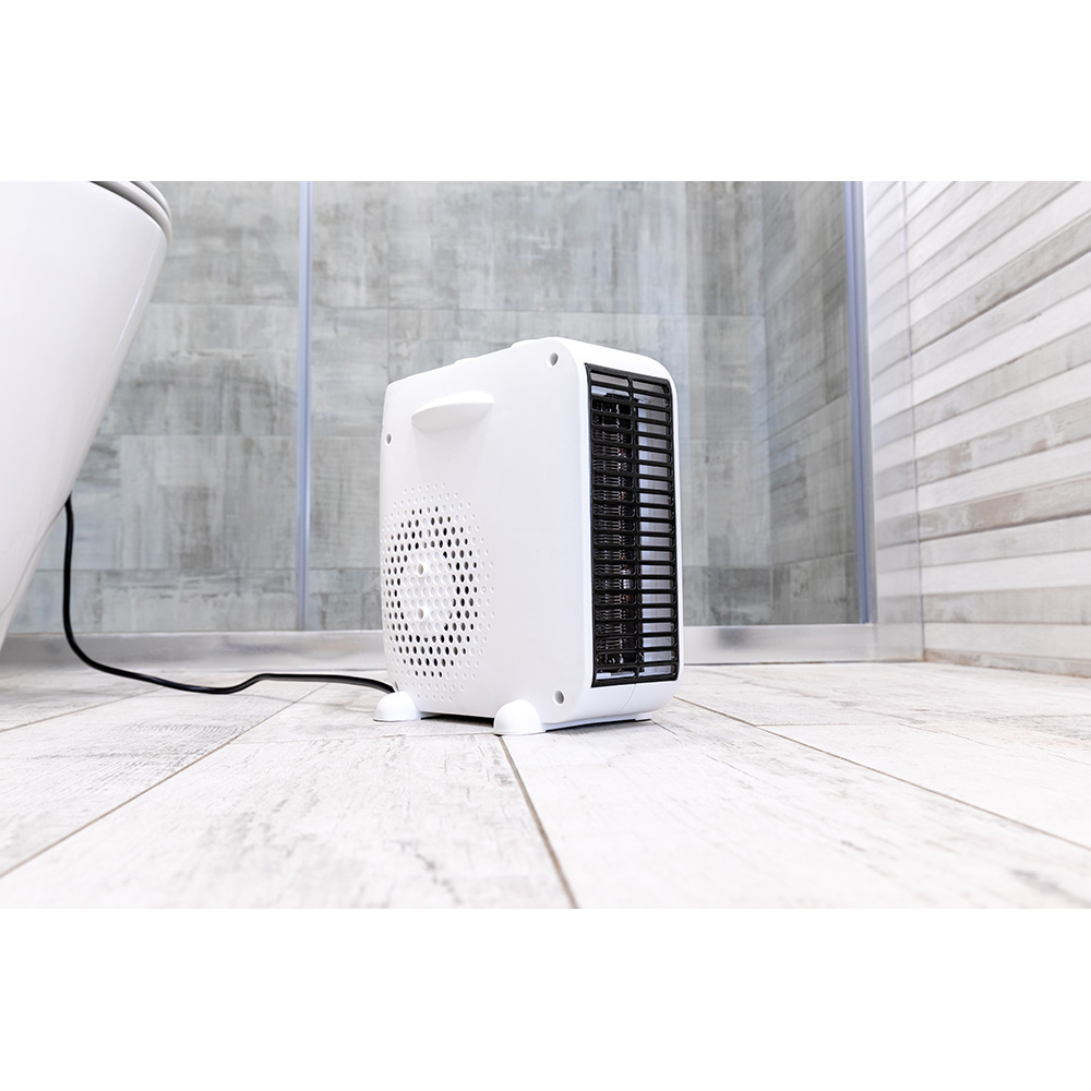 Un calentador eléctrico blanco en un suelo de madera, con un inodoro a la izquierda y una ducha al fondo.