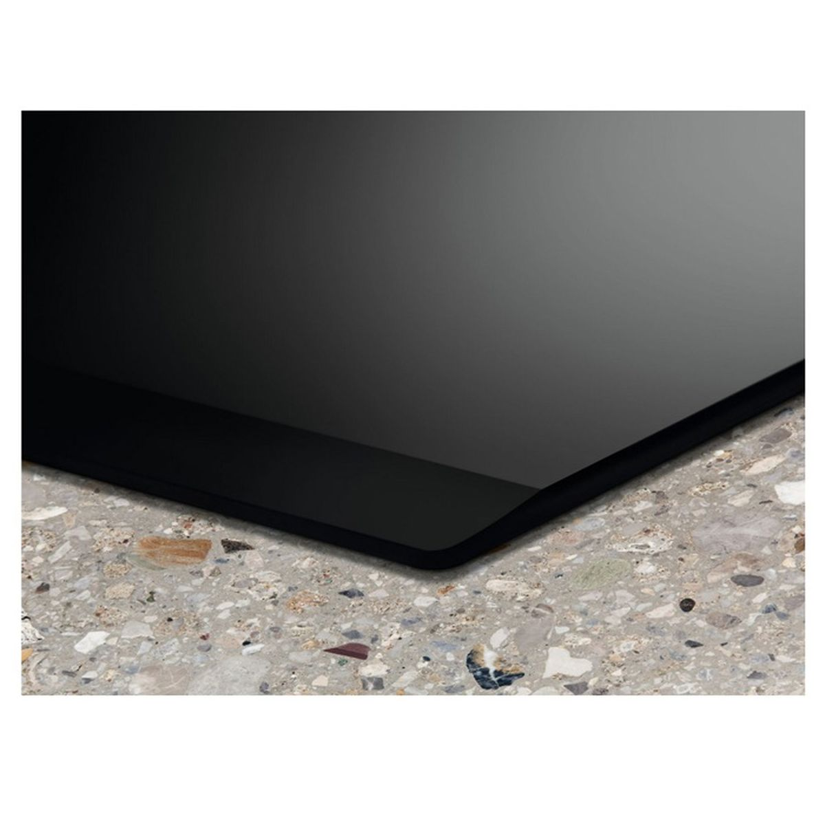 Primer plano de una superficie negra y reflectante, posiblemente vidrio, sobre una encimera gris moteada. El borde es visible.