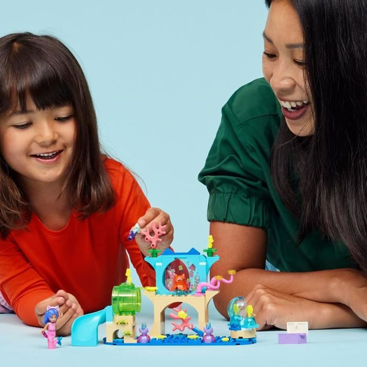 Dziewczynka i kobieta bawią się zestawem Lego przedstawiającym podwodną scenę, z kolorowymi klockami i figurkami.