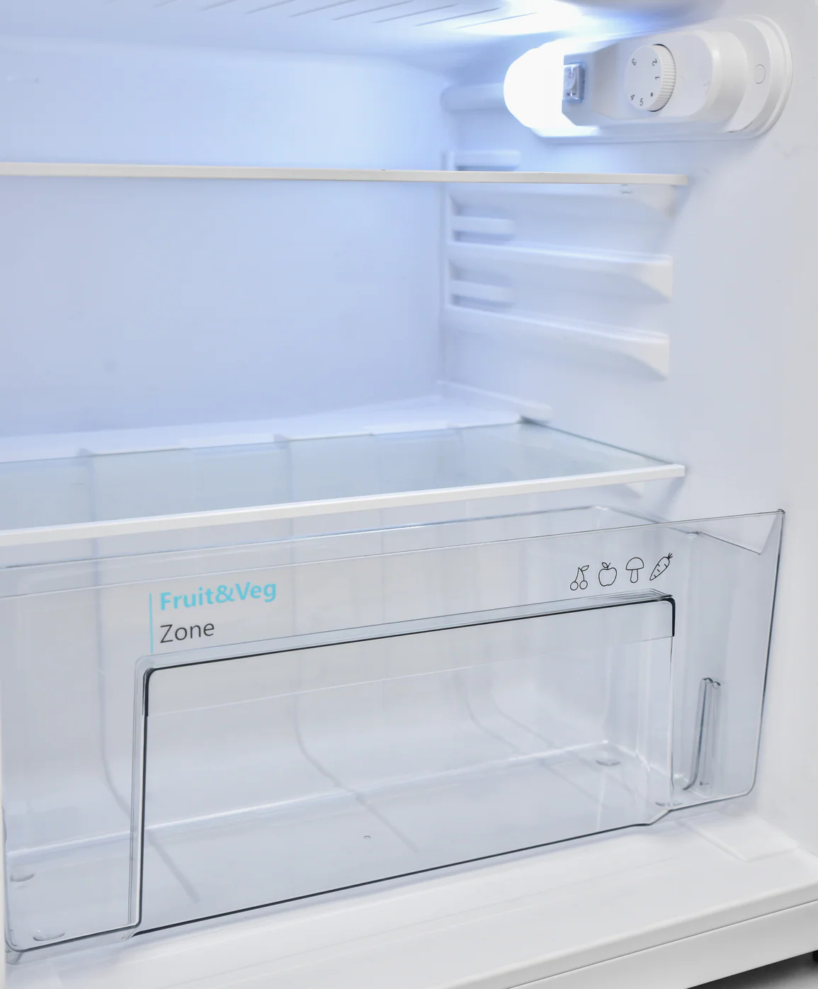 An empty white refrigerator interior. It has shelves and a fruit and vegetable zone. Light shines from the top.