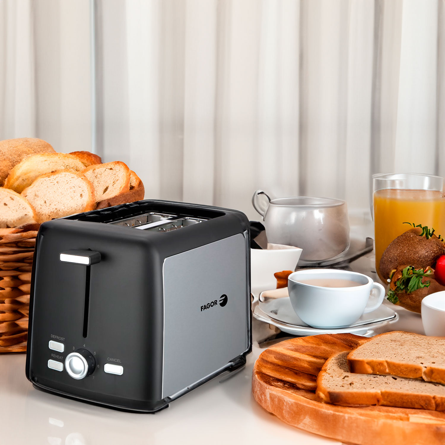 Ein Toaster, Brotscheiben, eine Tasse Tee, Orangensaft und andere Frühstücksartikel auf einem Tisch. Ein Brotkorb im Hintergrund.