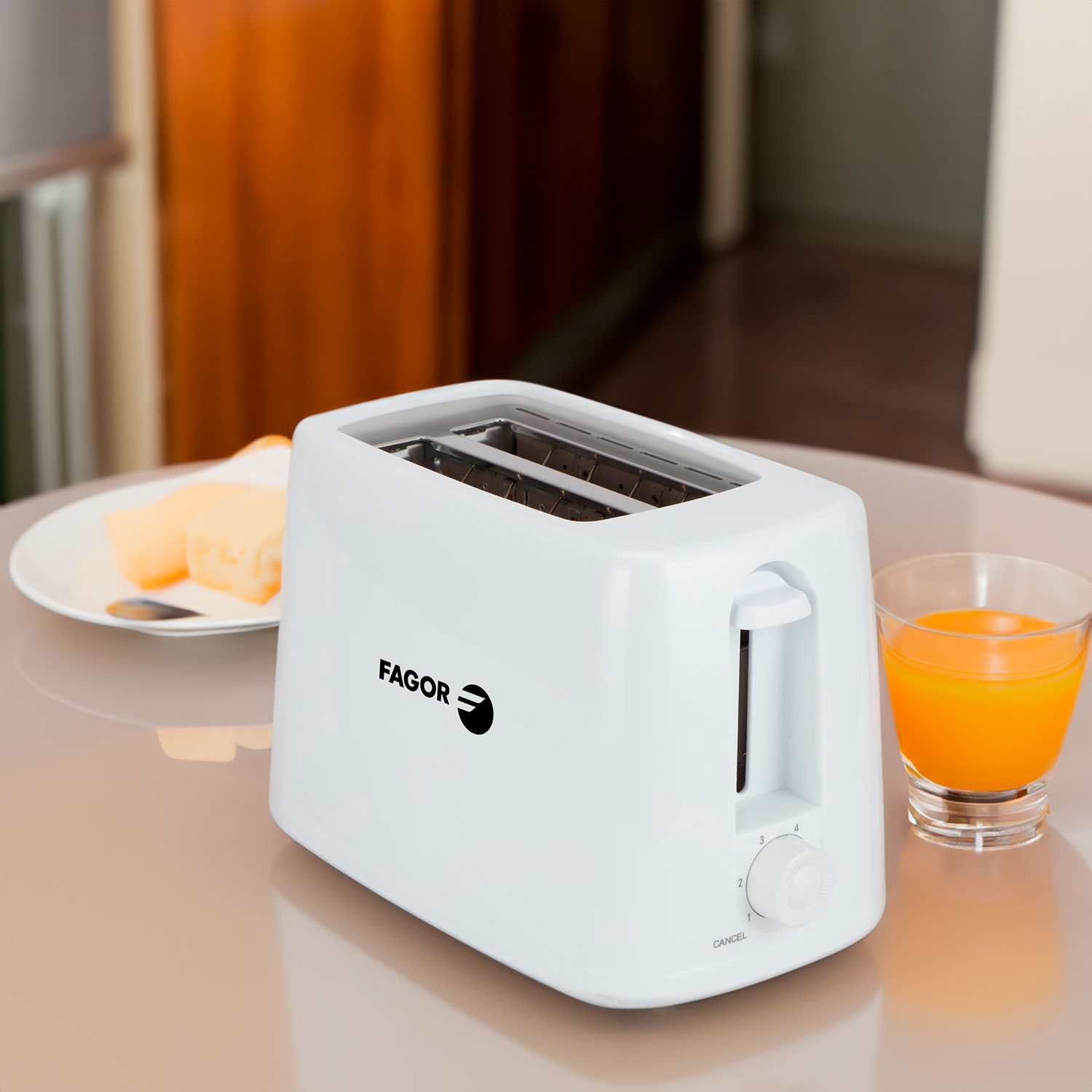 Weißer Fagor-Toaster auf einem Tisch neben einem Glas Orangensaft und einem Teller mit Butter. Im Hintergrund ist ein Raum mit Holz.