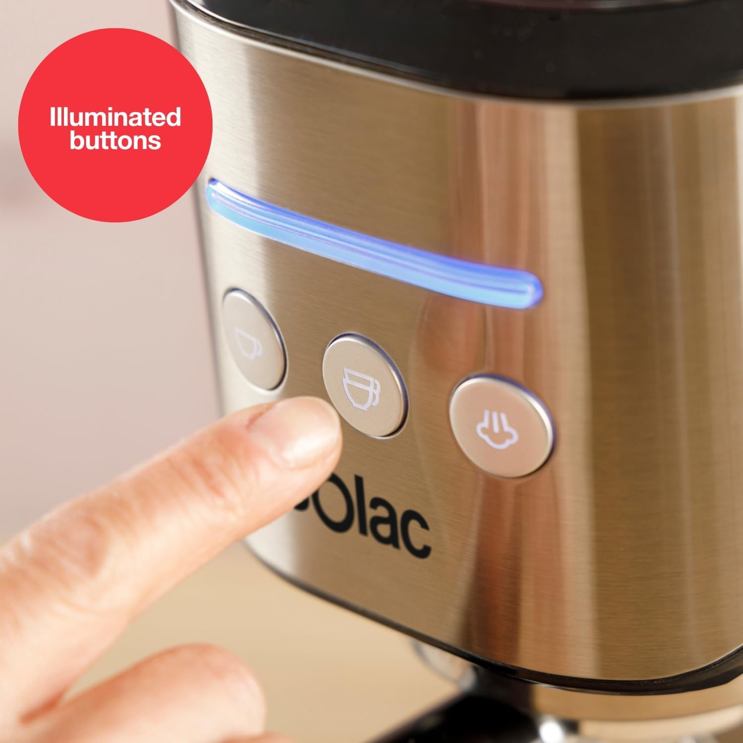 Una mano presiona un botón en una cafetera. Se ven botones iluminados y una luz azul. La máquina es plateada, con "Olac" escrito.