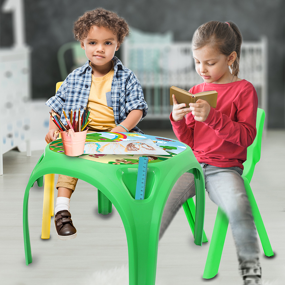 Zwei Kinder sitzen an einem grünen Tisch. Ein Kind hält Bleistifte, das andere liest ein Buch. Beide sitzen auf grünen Stühlen.