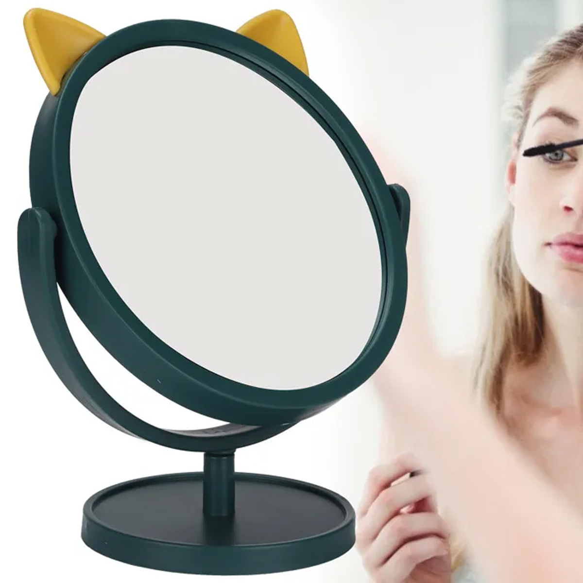 Ein grüner Spiegel mit Katzenohren steht auf einem Tisch, im Hintergrund trägt eine Frau Mascara auf.